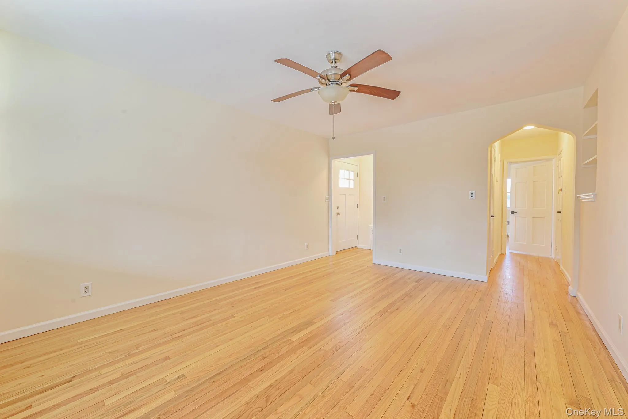 Unfurnished room featuring arched walkways, light wood-style floors, and ceiling fan Unfurnished room featuring arched walkways, light wood-style floors, and ceiling fan