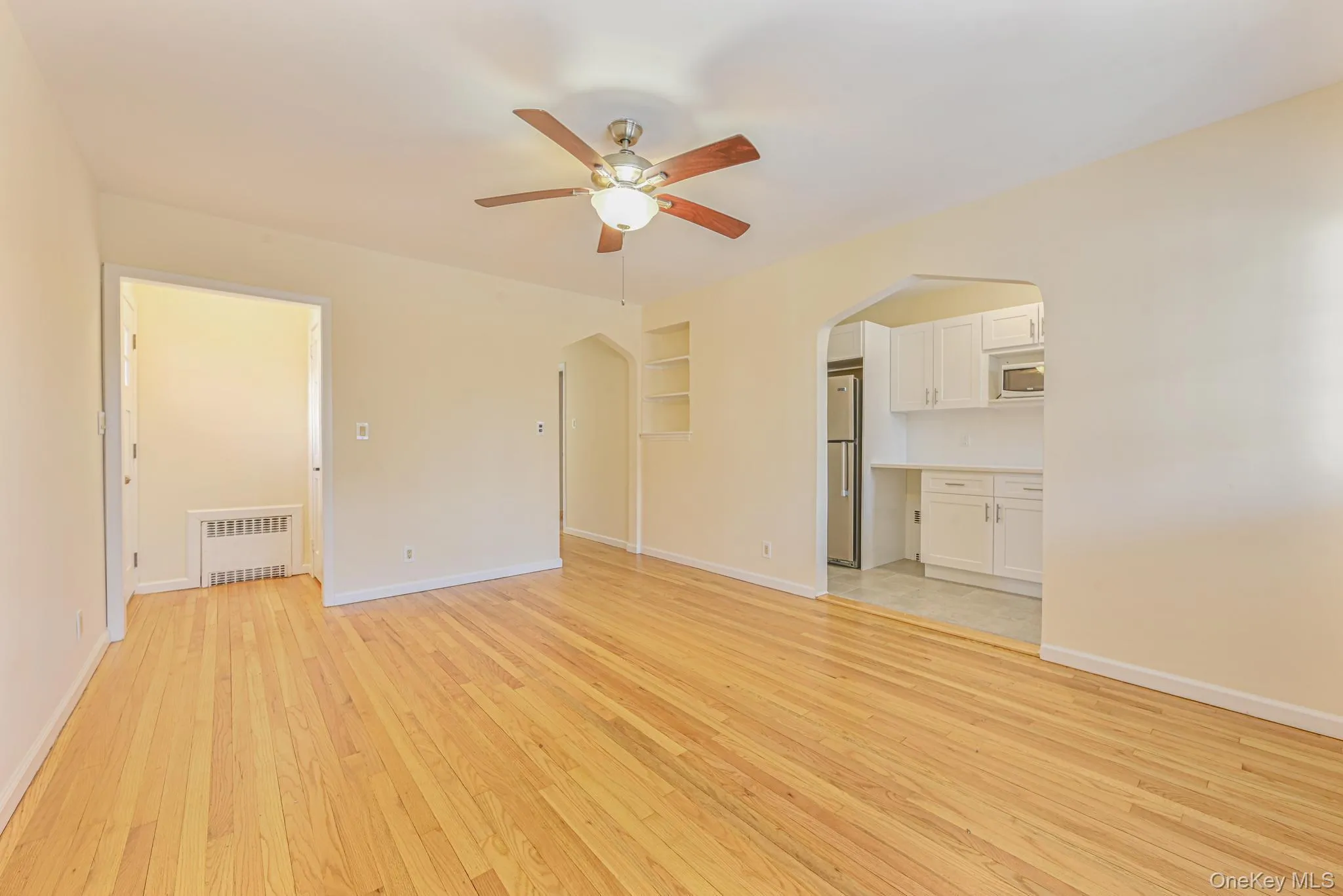 Unfurnished living room featuring arched walkways, light wood finished floors, radiator, and a ceiling fan Unfurnished living room featuring arched walkways, light wood finished floors, radiator, and a ceiling fan