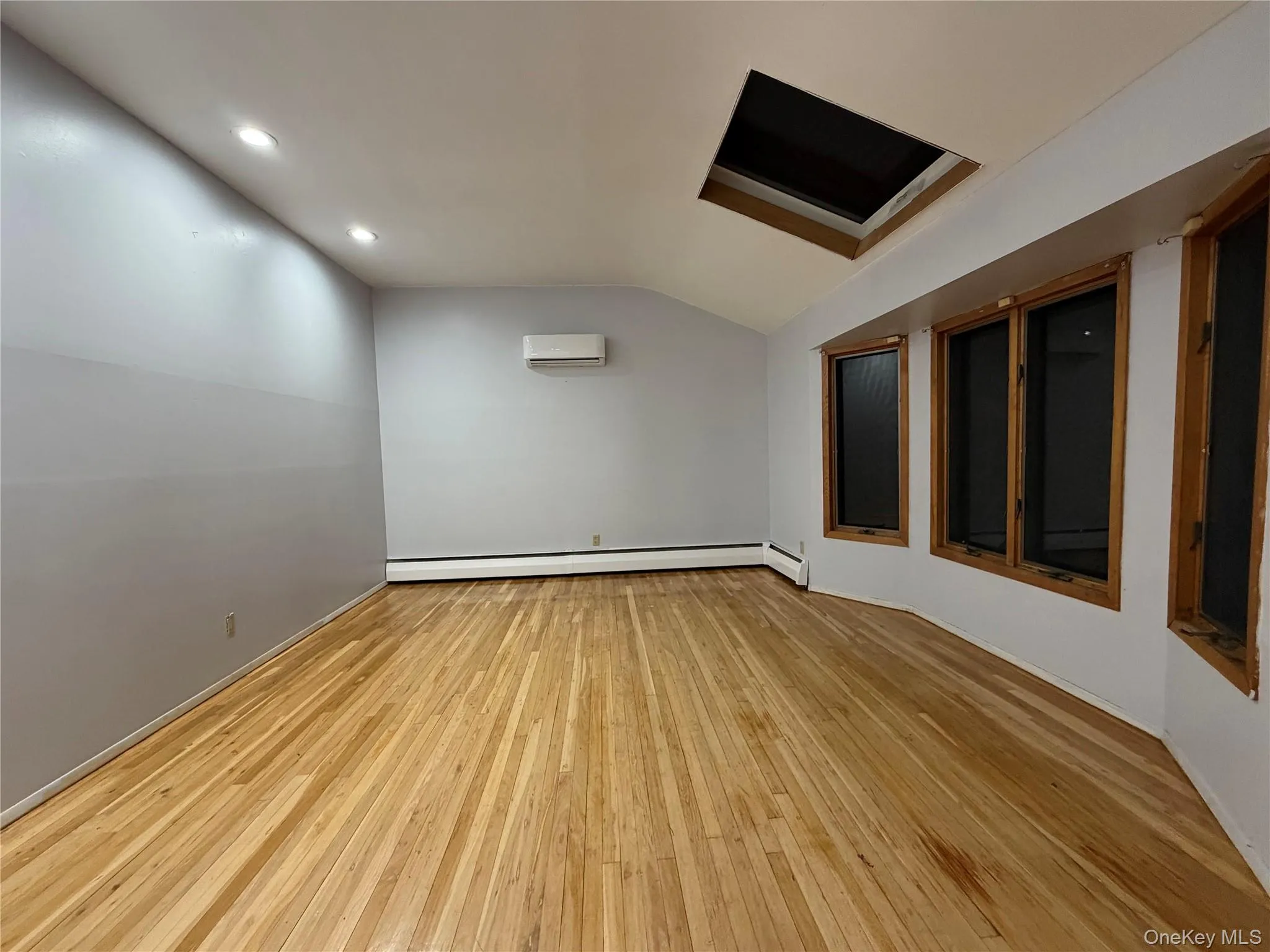 Unfurnished room featuring lofted ceiling, light wood-style flooring, recessed lighting, and baseboard heating Unfurnished room featuring lofted ceiling, light wood-style flooring, recessed lighting, and baseboard heating
