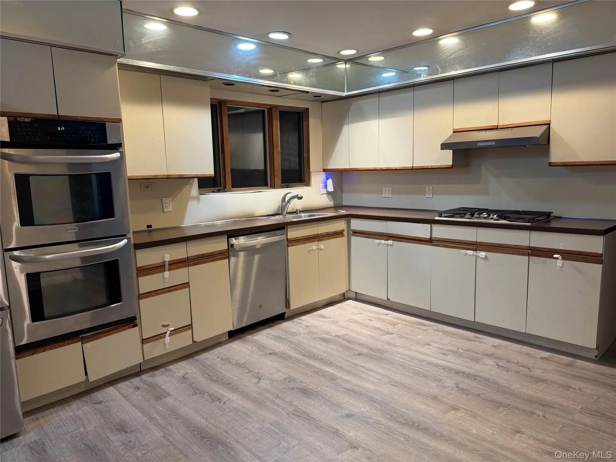 Kitchen featuring recessed lighting, stainless steel appliances, light wood-type flooring, dark countertops, and under cabinet range hood Kitchen featuring recessed lighting, stainless steel appliances, light wood-type flooring, dark countertops, and under cabinet range hood
