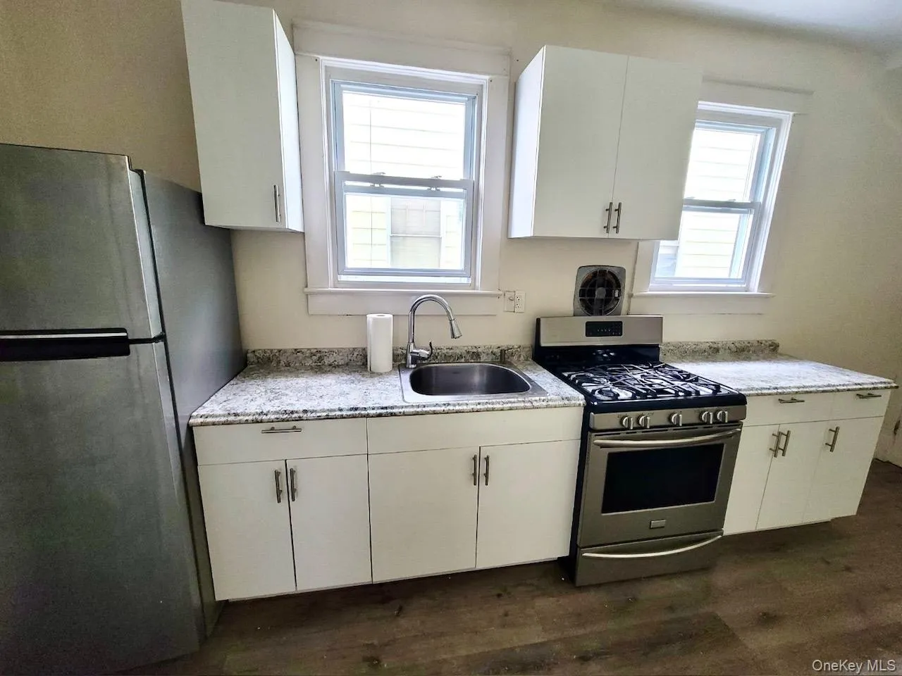 Kitchen featuring stainless steel appliances, white cabinetry, light stone countertops, and dark wood finished floors Kitchen featuring stainless steel appliances, white cabinetry, light stone countertops, and dark wood finished floors