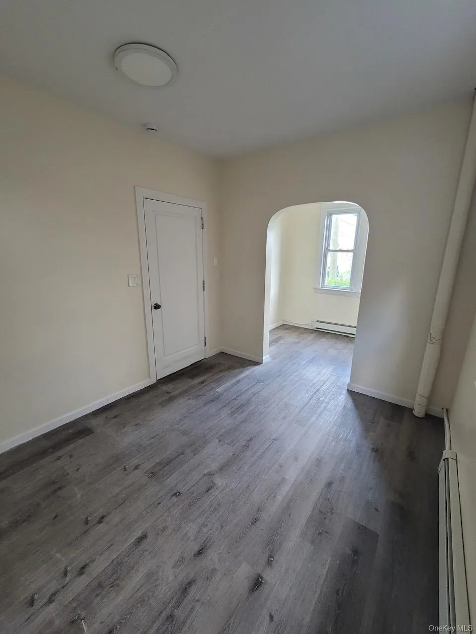 Spare room featuring arched walkways, a baseboard radiator, dark wood-type flooring, and a baseboard heating unit Spare room featuring arched walkways, a baseboard radiator, dark wood-type flooring, and a baseboard heating unit