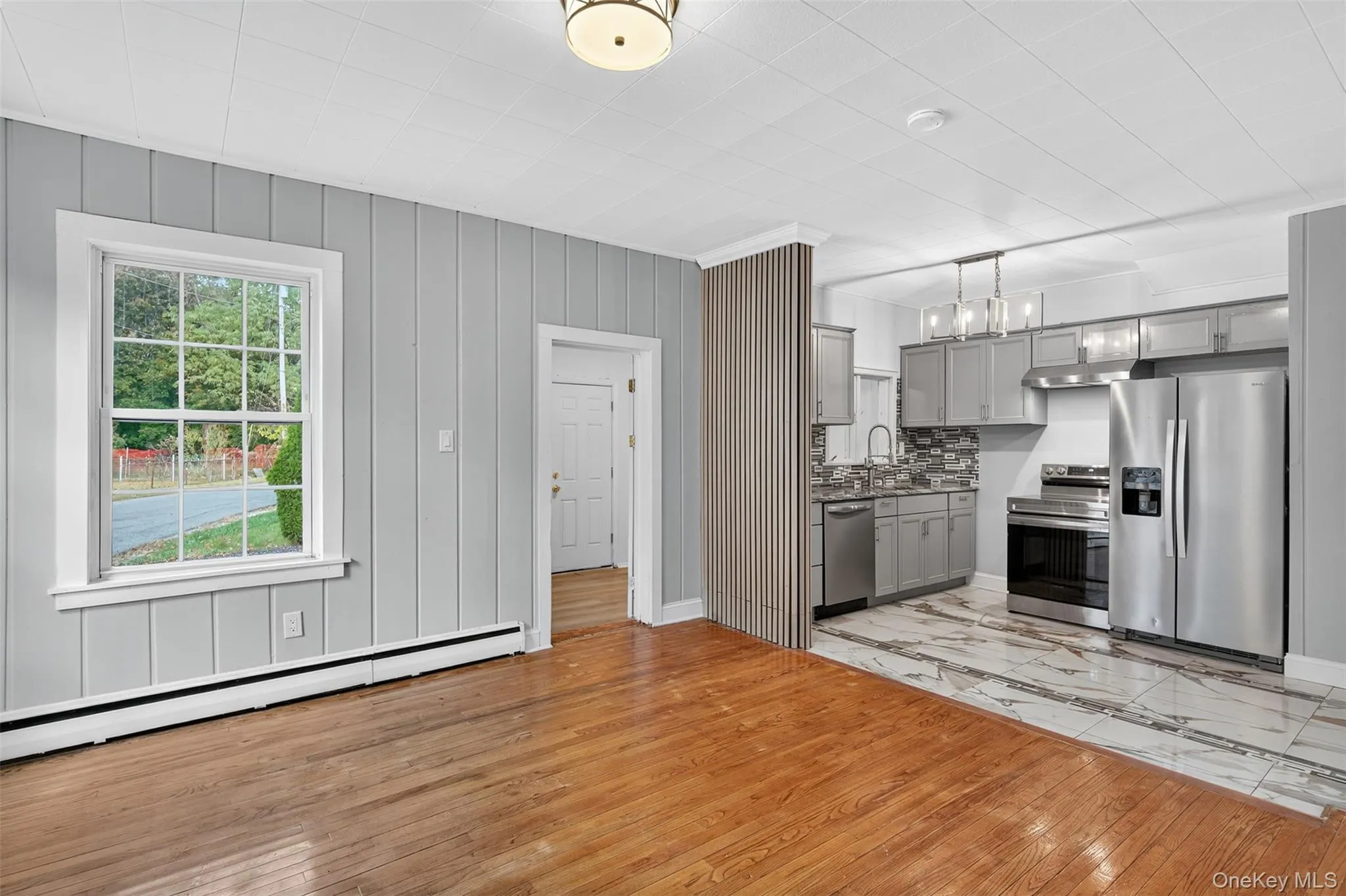 Kitchen featuring gray cabinetry, light wood-type flooring, appliances with stainless steel finishes, pendant lighting, and a baseboard heating unit Kitchen featuring gray cabinetry, light wood-type flooring, appliances with stainless steel finishes, pendant lighting, and a baseboard heating unit