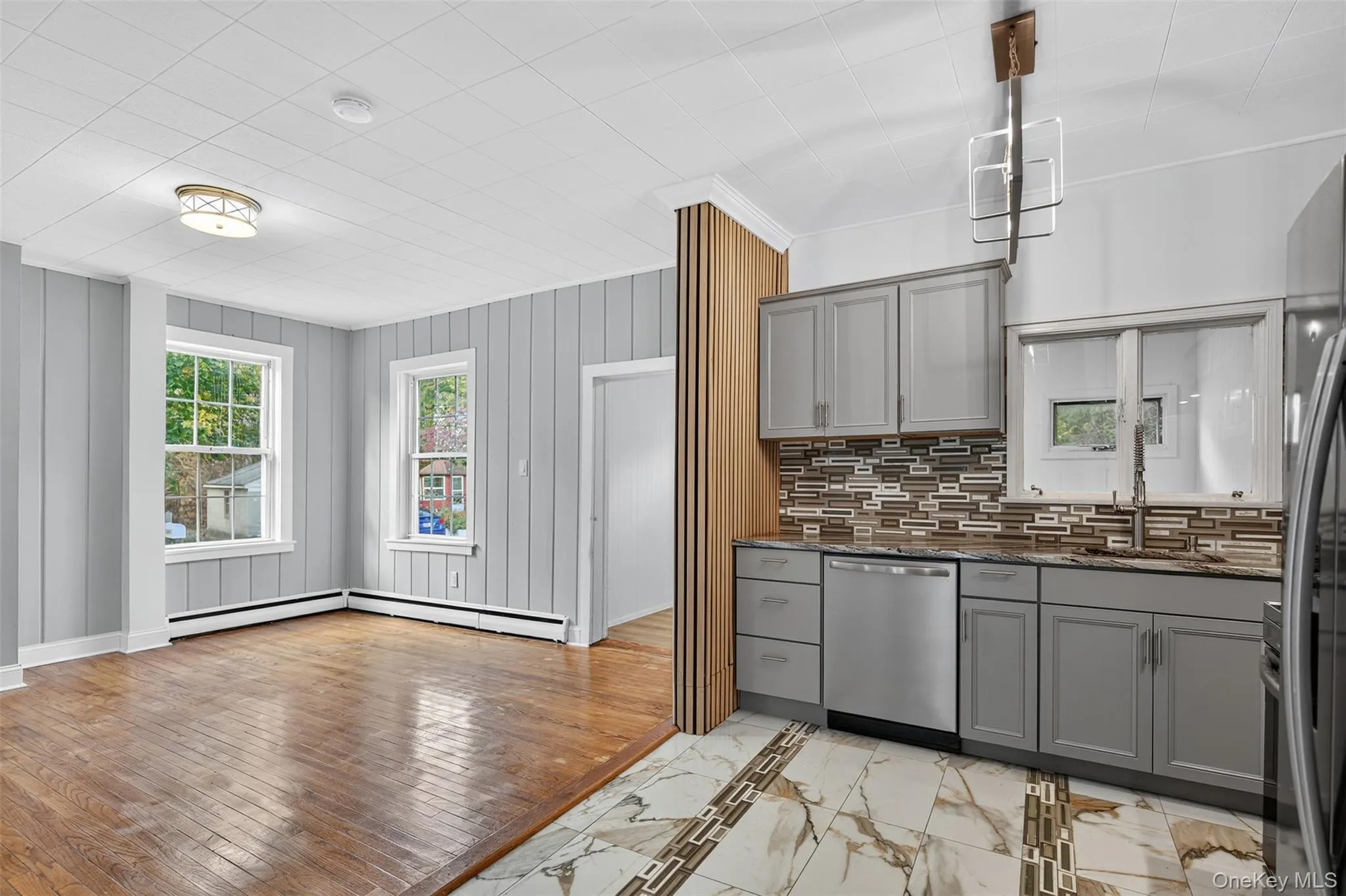 Kitchen with gray cabinets, light marble finish floors, stainless steel appliances, dark stone counters, and backsplash Kitchen with gray cabinets, light marble finish floors, stainless steel appliances, dark stone counters, and backsplash