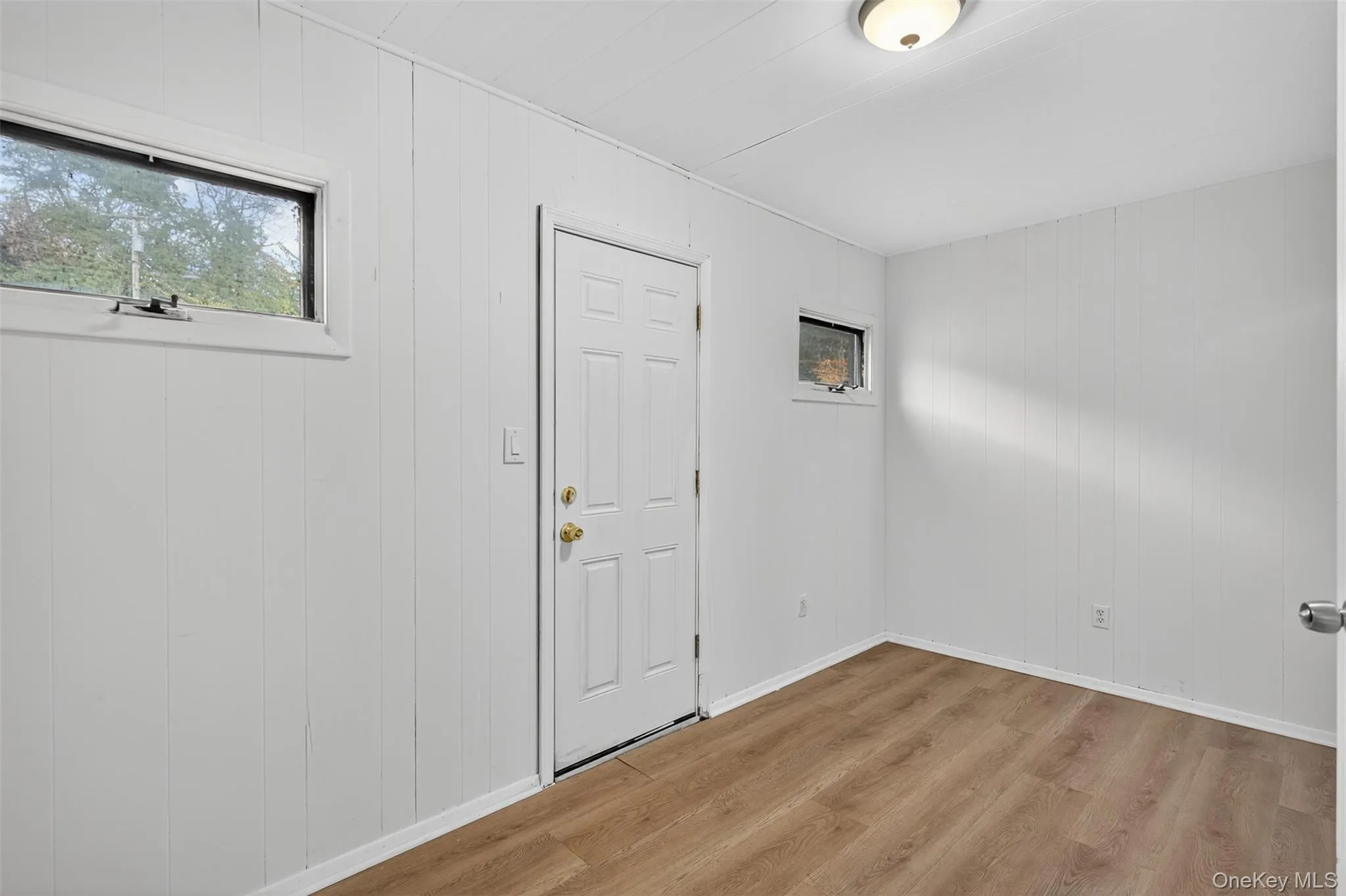 Unfurnished room featuring light wood finished floors, plenty of natural light, and wood walls Unfurnished room featuring light wood finished floors, plenty of natural light, and wood walls