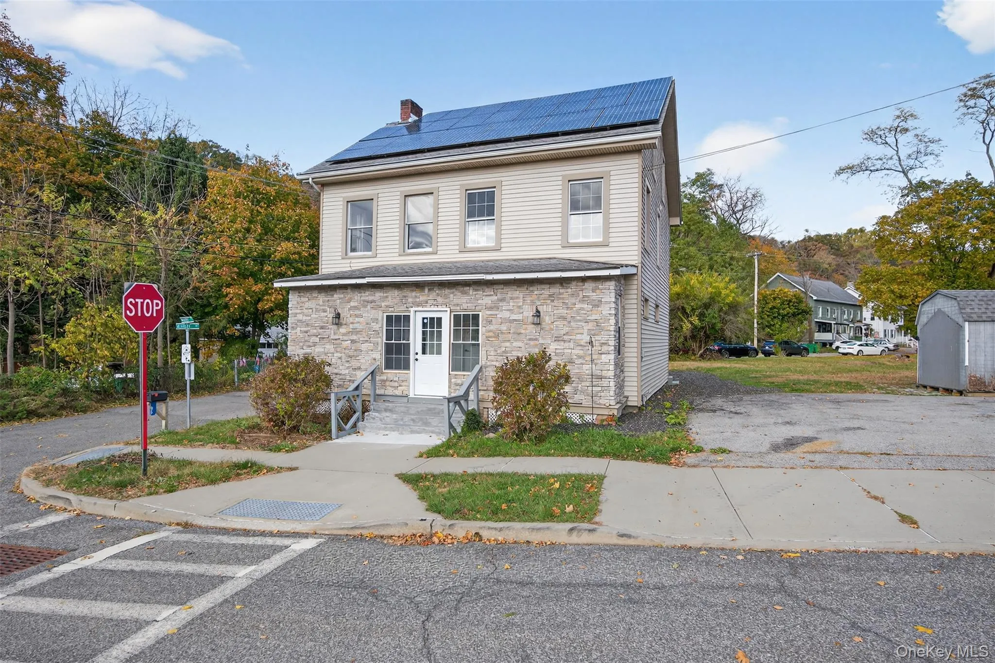 View of front facade with roof mounted solar panels, stone siding, and a chimney View of front facade with roof mounted solar panels, stone siding, and a chimney