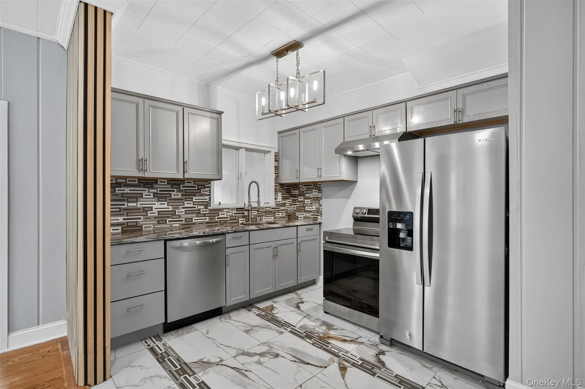 Kitchen with gray cabinets, appliances with stainless steel finishes, light marble finish flooring, dark stone counters, and hanging light fixtures Kitchen with gray cabinets, appliances with stainless steel finishes, light marble finish flooring, dark stone counters, and hanging light fixtures