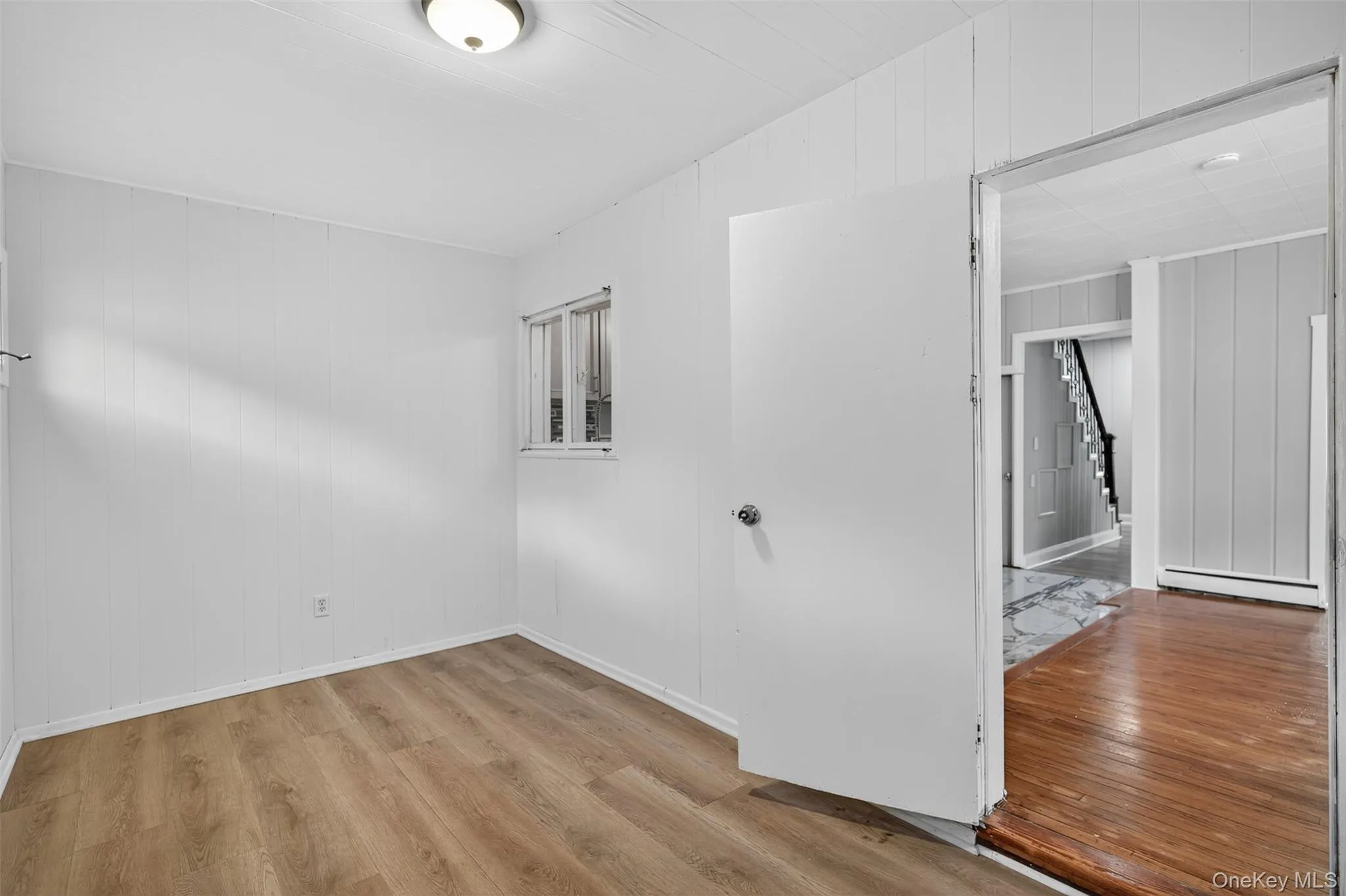 Empty room with light wood-style flooring, wooden walls, and a baseboard radiator Empty room with light wood-style flooring, wooden walls, and a baseboard radiator