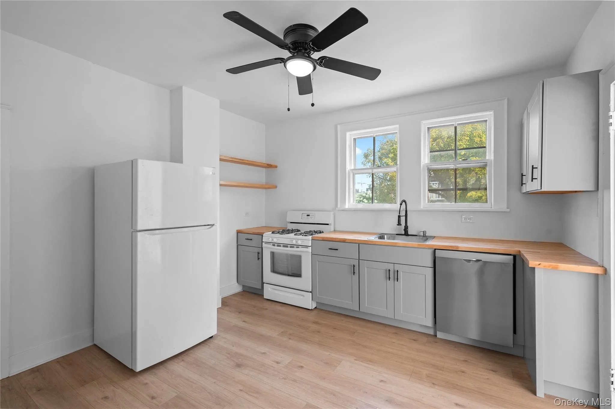 Kitchen with white appliances, open shelves, butcher block countertops, light wood-style flooring, and a ceiling fan Kitchen with white appliances, open shelves, butcher block countertops, light wood-style flooring, and a ceiling fan
