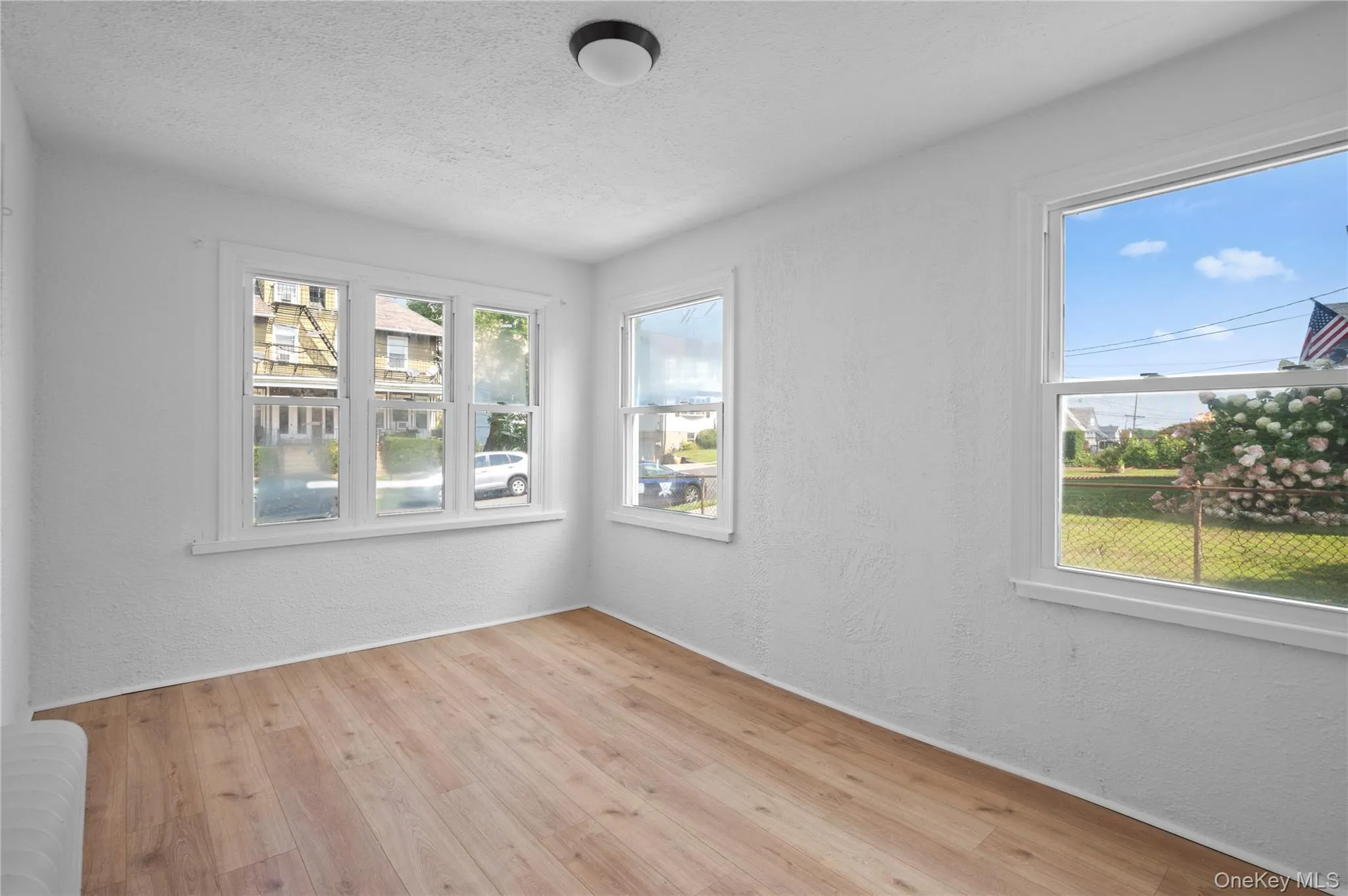 Spare room featuring a textured wall, radiator heating unit, light wood-type flooring, and a textured ceiling Spare room featuring a textured wall, radiator heating unit, light wood-type flooring, and a textured ceiling