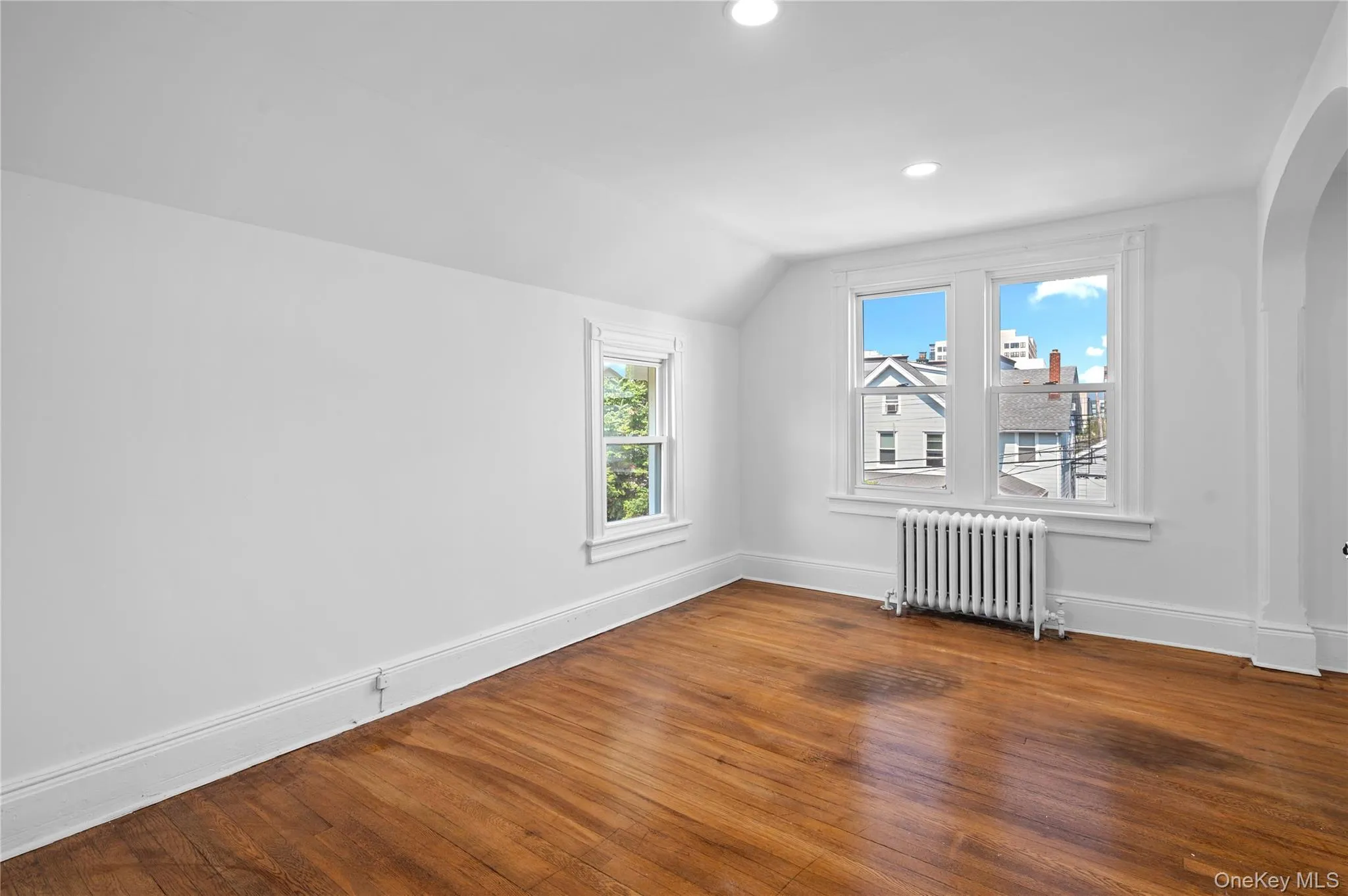 Bonus room featuring radiator heating unit, hardwood / wood-style floors, lofted ceiling, arched walkways, and recessed lighting Bonus room featuring radiator heating unit, hardwood / wood-style floors, lofted ceiling, arched walkways, and recessed lighting