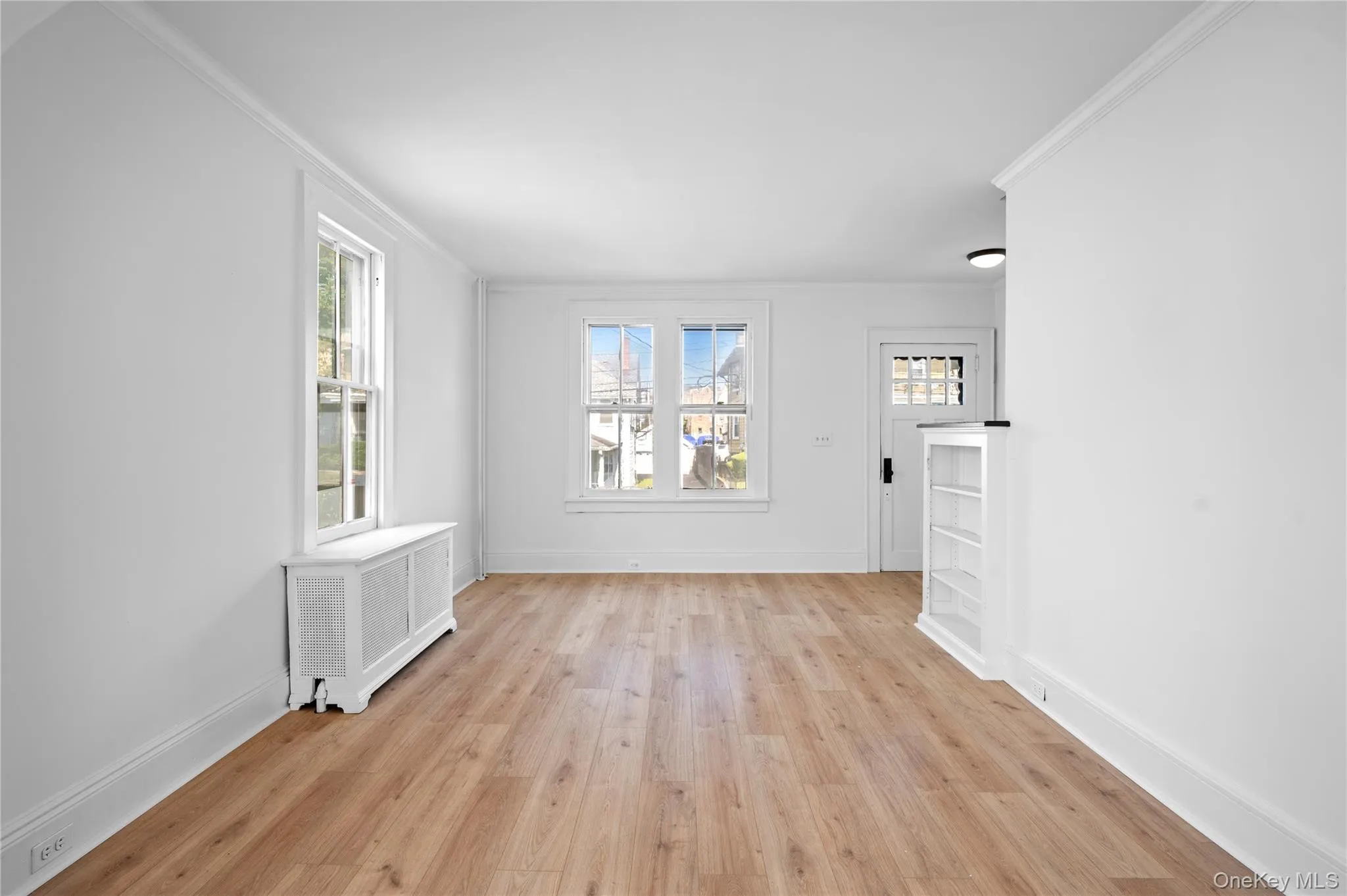Unfurnished living room featuring radiator, light wood-style floors, healthy amount of natural light, and crown molding Unfurnished living room featuring radiator, light wood-style floors, healthy amount of natural light, and crown molding