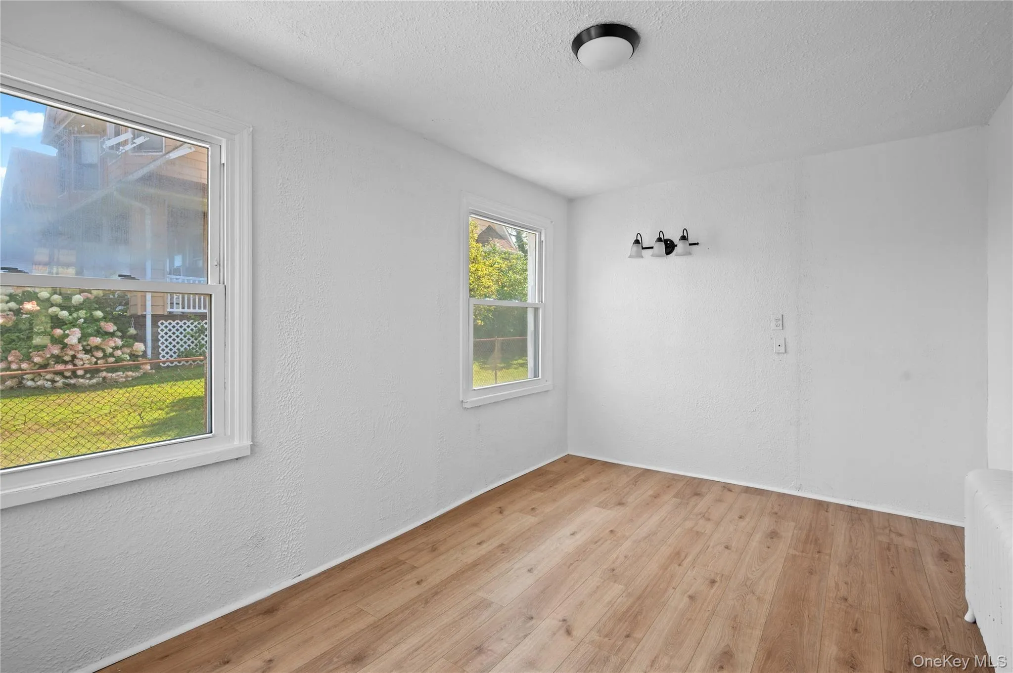 Empty room with a textured wall, a textured ceiling, light wood-style floors, and radiator heating unit Empty room with a textured wall, a textured ceiling, light wood-style floors, and radiator heating unit