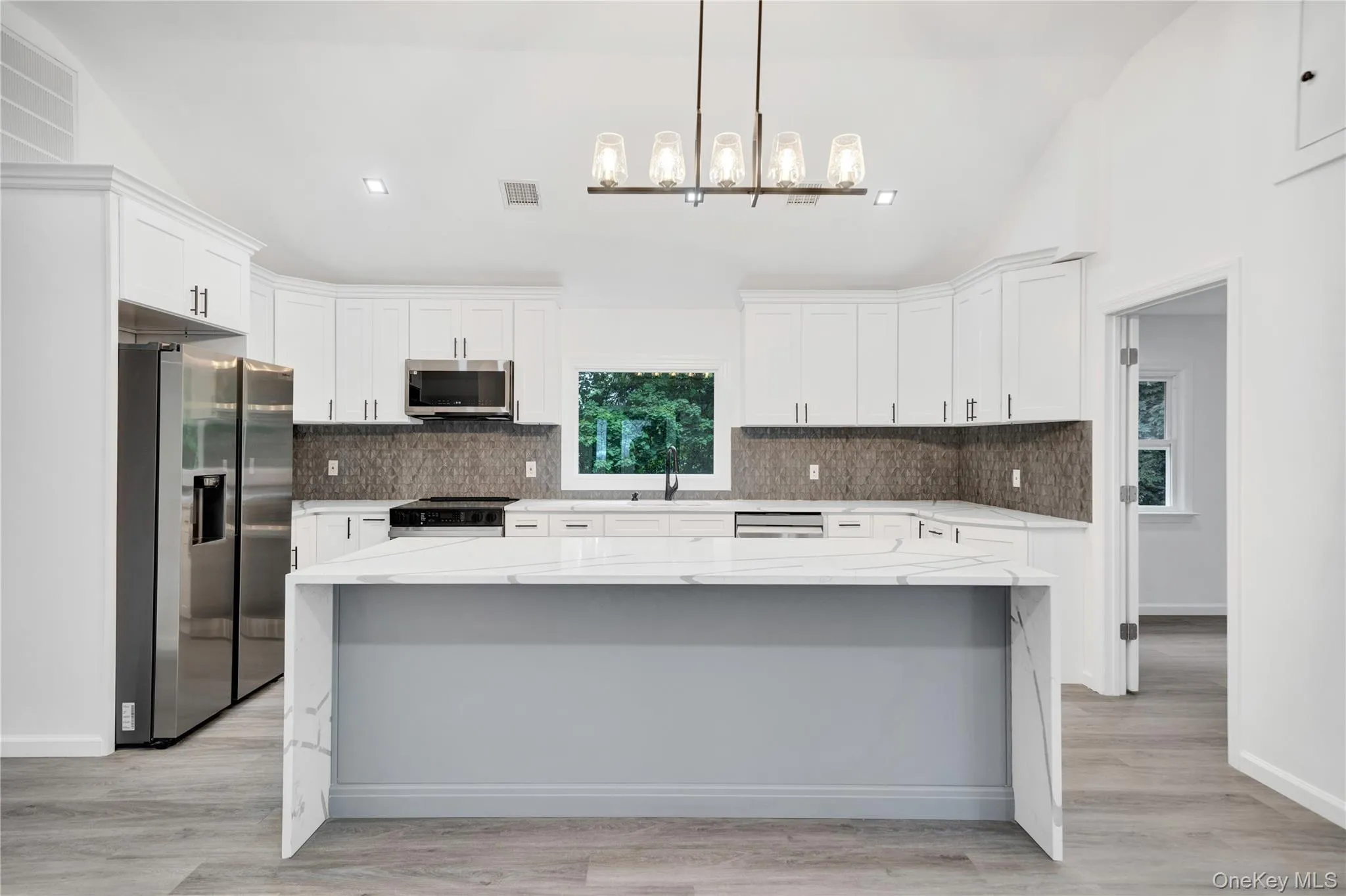 Kitchen with vaulted ceiling, light stone counters, stainless steel appliances, white cabinets, and a kitchen island Kitchen with vaulted ceiling, light stone counters, stainless steel appliances, white cabinets, and a kitchen island