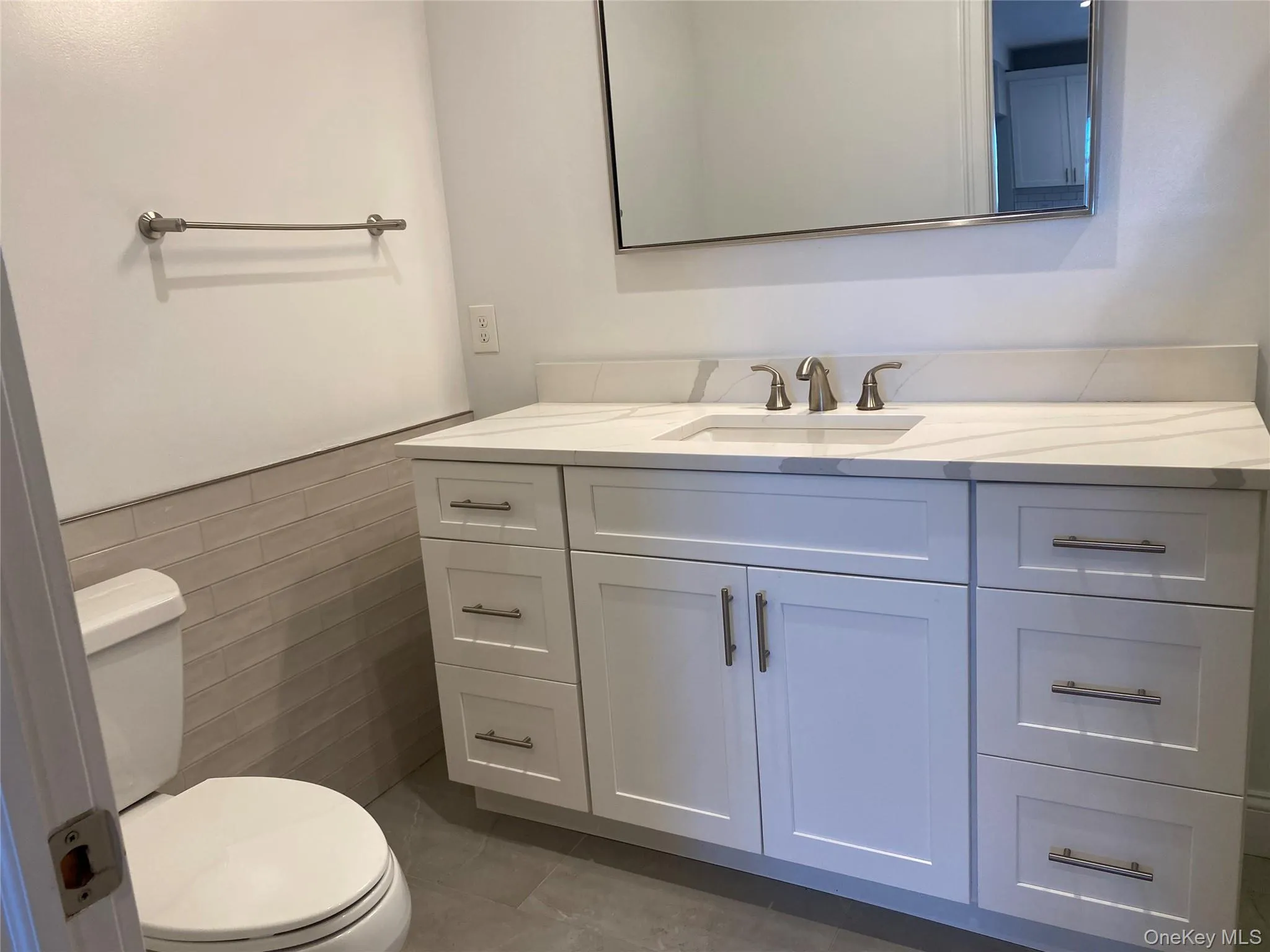 Half bath featuring tile walls, vanity, a wainscoted wall, and dark tile patterned floors Half bath featuring tile walls, vanity, a wainscoted wall, and dark tile patterned floors