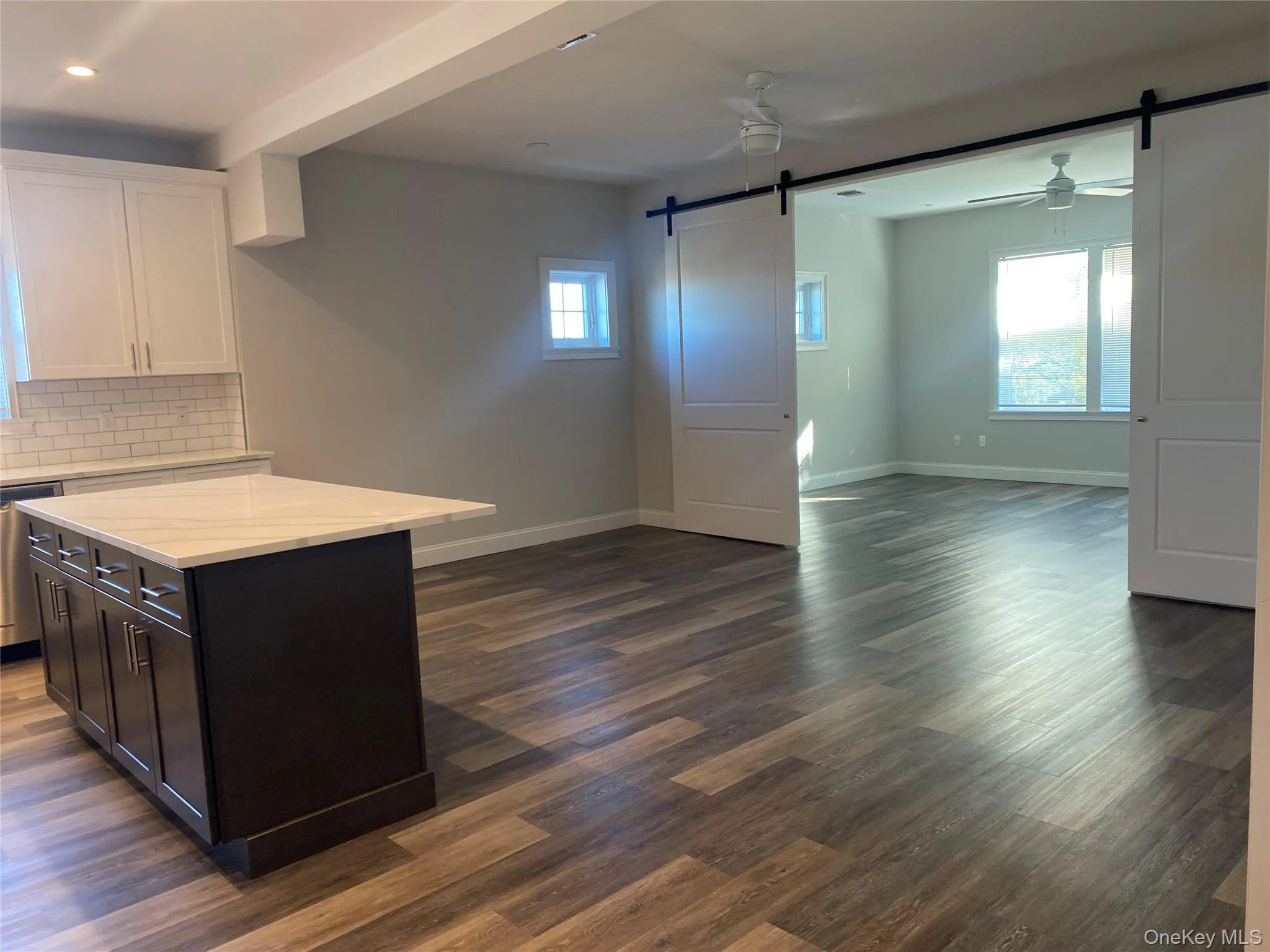 Kitchen featuring a barn door, ceiling fan, white cabinets, tasteful backsplash, and a center island Kitchen featuring a barn door, ceiling fan, white cabinets, tasteful backsplash, and a center island