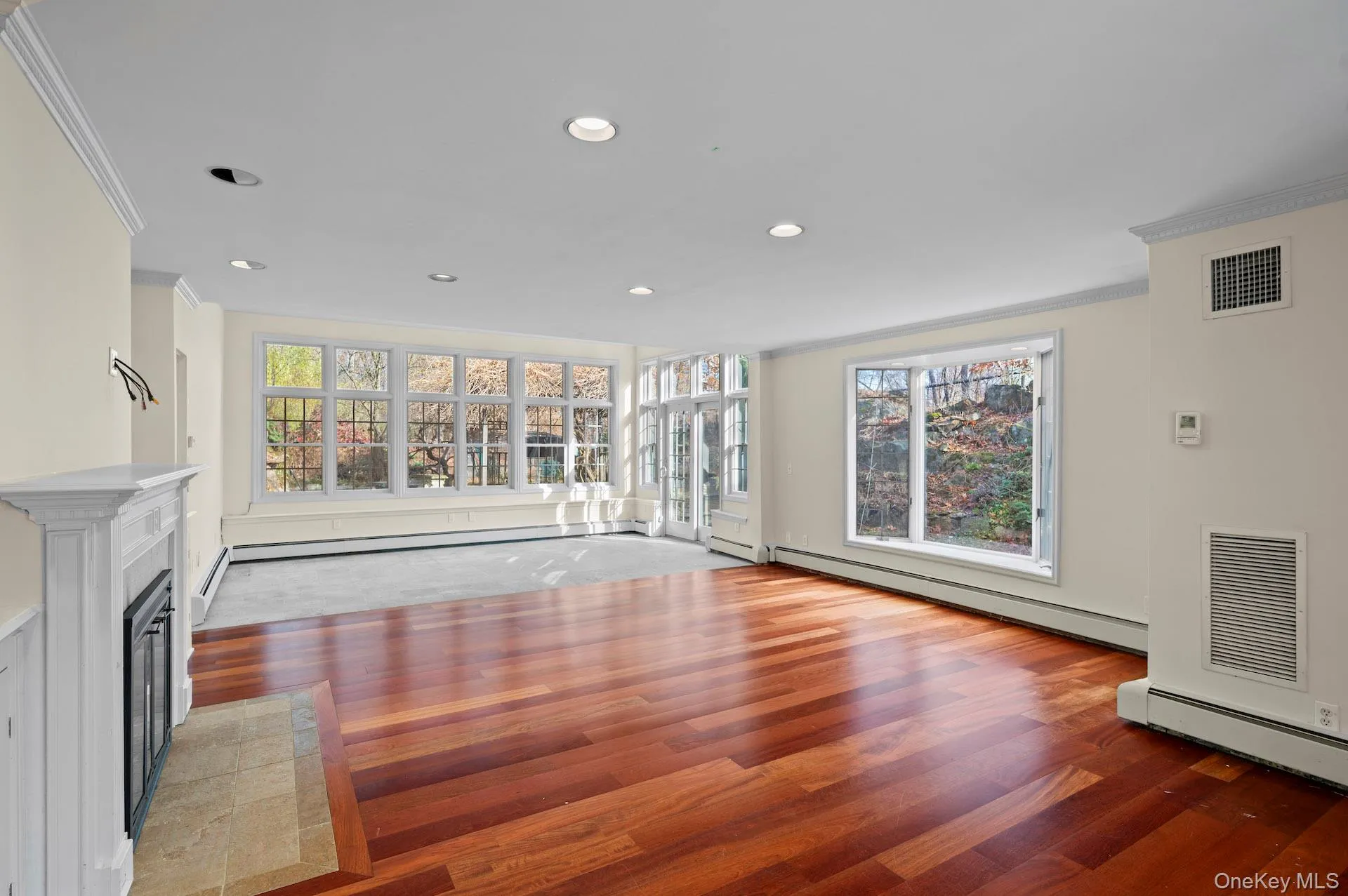 Unfurnished living room with crown molding, a tile fireplace, baseboard heating, recessed lighting, and wood-type flooring Unfurnished living room with crown molding, a tile fireplace, baseboard heating, recessed lighting, and wood-type flooring