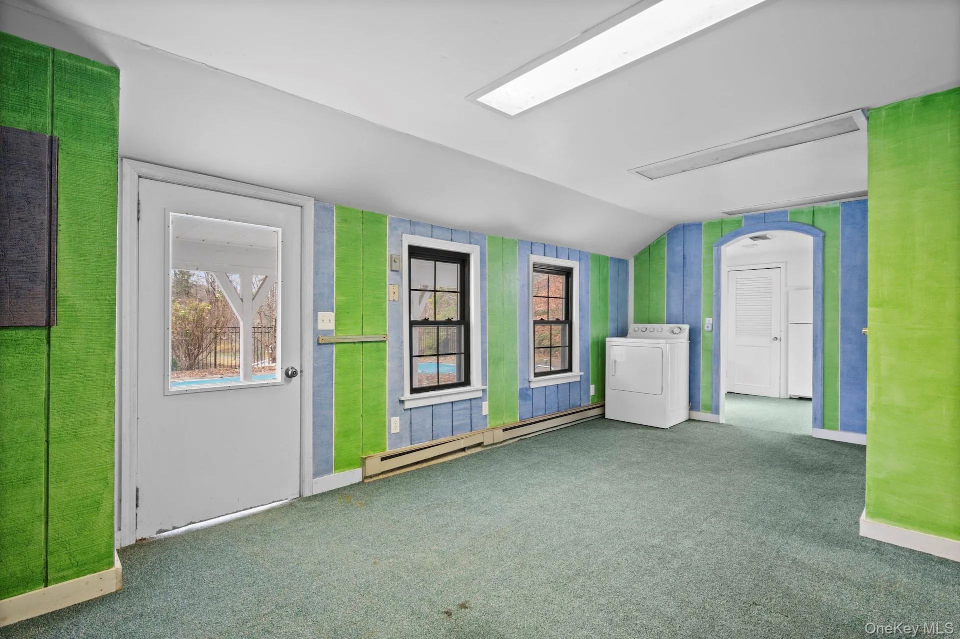 Unfurnished room featuring vaulted ceiling, washer / clothes dryer, a baseboard radiator, and carpet Unfurnished room featuring vaulted ceiling, washer / clothes dryer, a baseboard radiator, and carpet