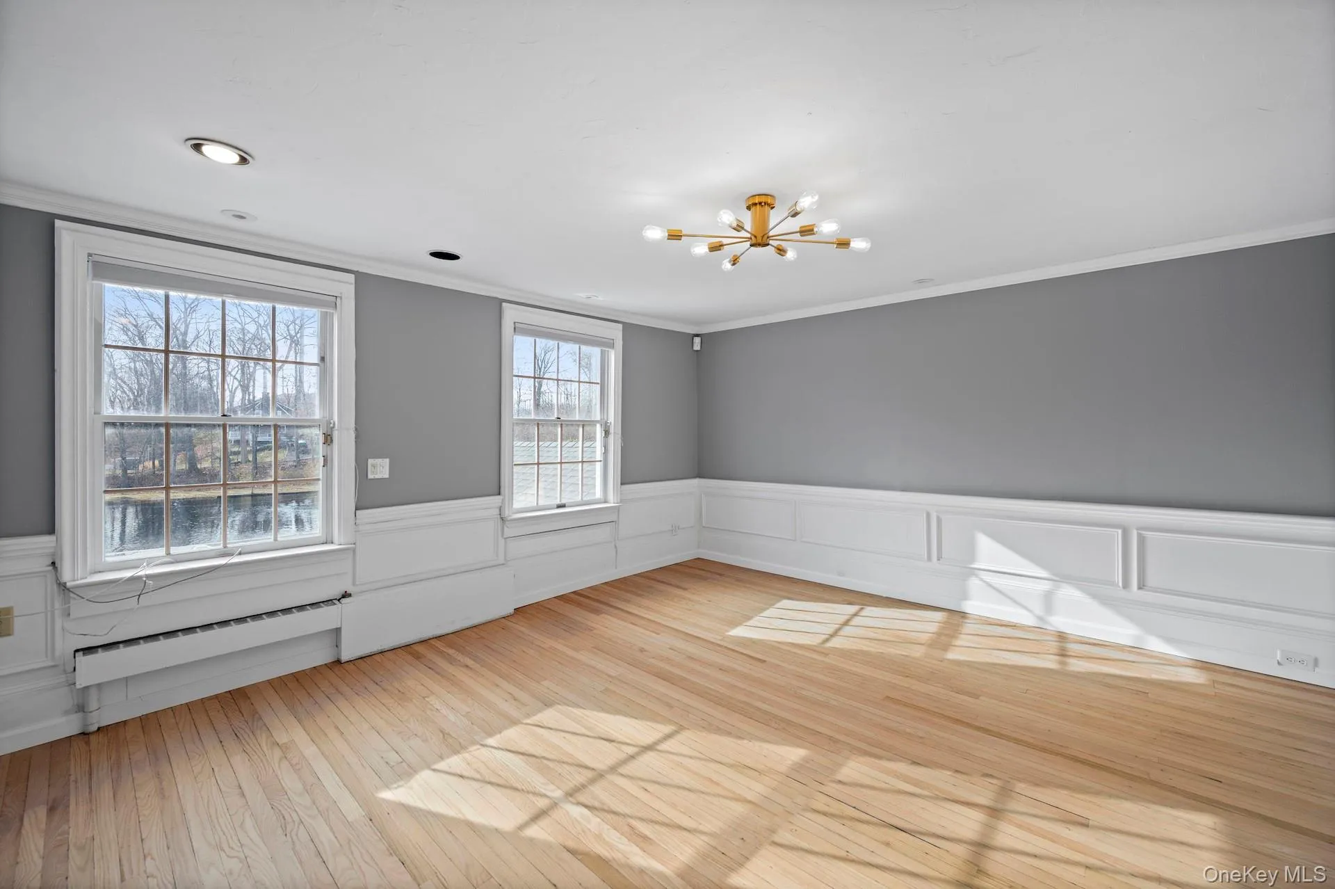 Spare room with wainscoting, a chandelier, light wood-style flooring, crown molding, and baseboard heating Spare room with wainscoting, a chandelier, light wood-style flooring, crown molding, and baseboard heating