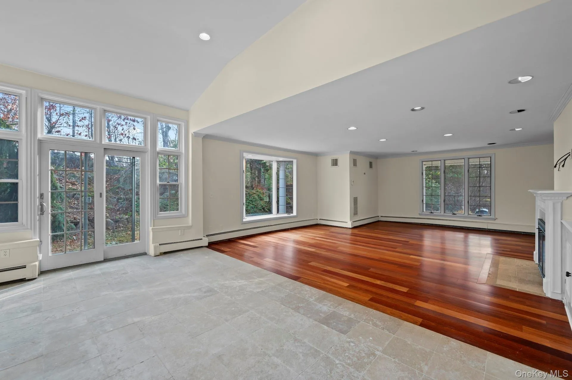 Unfurnished living room featuring hardwood / wood-style flooring, recessed lighting, a fireplace, lofted ceiling, and a baseboard radiator Unfurnished living room featuring hardwood / wood-style flooring, recessed lighting, a fireplace, lofted ceiling, and a baseboard radiator