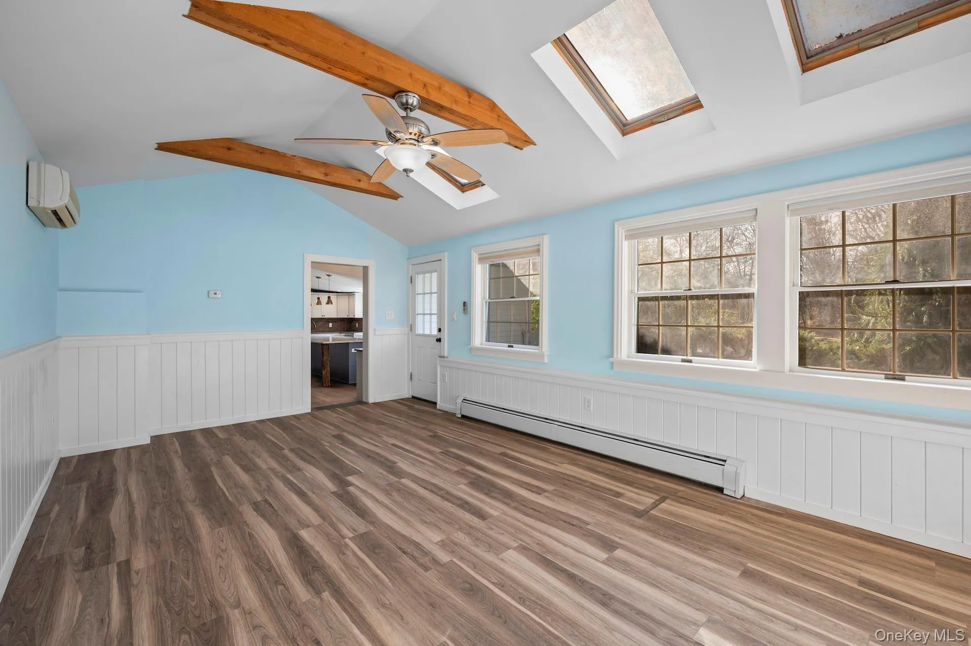 Spare room with a wainscoted wall, a baseboard heating unit, wood finished floors, a wall mounted air conditioner, and a skylight Spare room with a wainscoted wall, a baseboard heating unit, wood finished floors, a wall mounted air conditioner, and a skylight