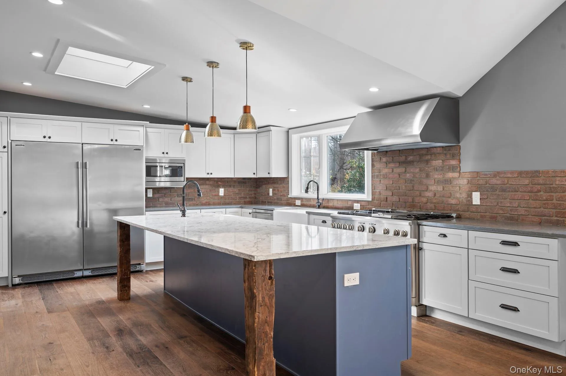 Kitchen featuring an island with sink, built in appliances, a skylight, white cabinetry, and lofted ceiling Kitchen featuring an island with sink, built in appliances, a skylight, white cabinetry, and lofted ceiling