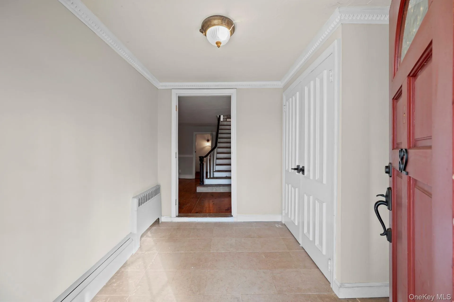 Corridor featuring radiator heating unit, a baseboard radiator, stairs, light tile patterned flooring, and crown molding Corridor featuring radiator heating unit, a baseboard radiator, stairs, light tile patterned flooring, and crown molding