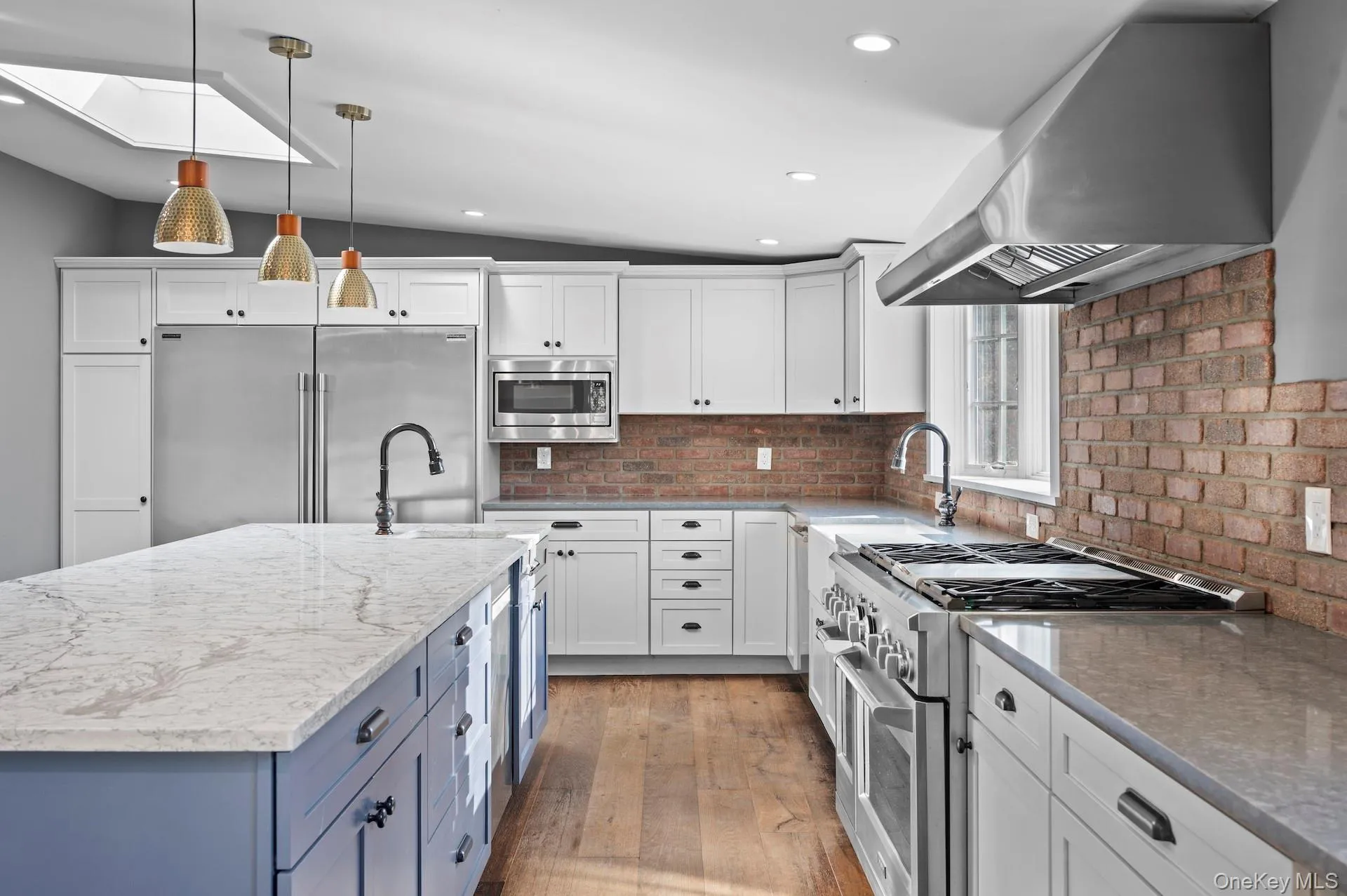 Kitchen with built in appliances, pendant lighting, range hood, light stone counters, and a kitchen island with sink Kitchen with built in appliances, pendant lighting, range hood, light stone counters, and a kitchen island with sink