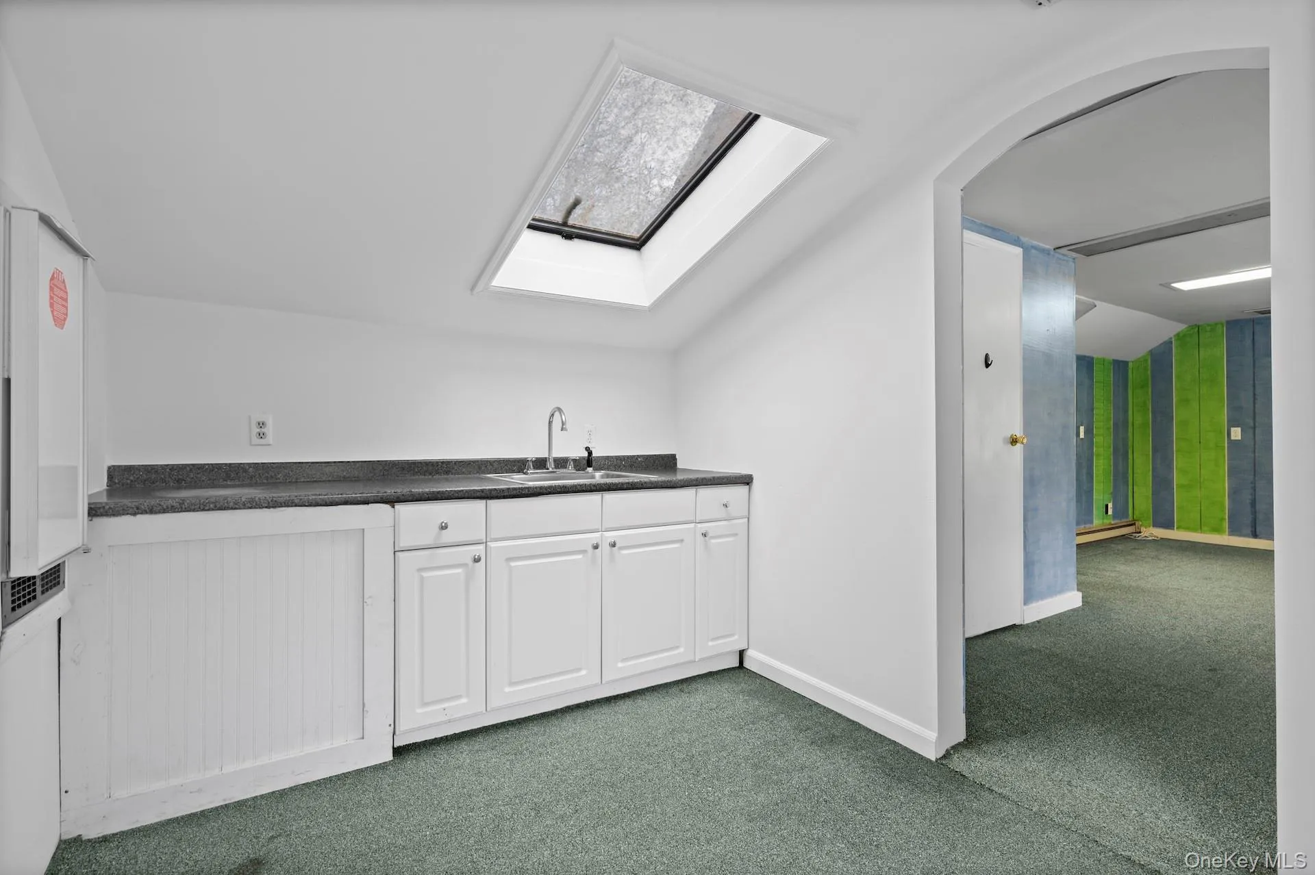 Bar featuring dark countertops, dark colored carpet, white cabinets, lofted ceiling, and a skylight Bar featuring dark countertops, dark colored carpet, white cabinets, lofted ceiling, and a skylight
