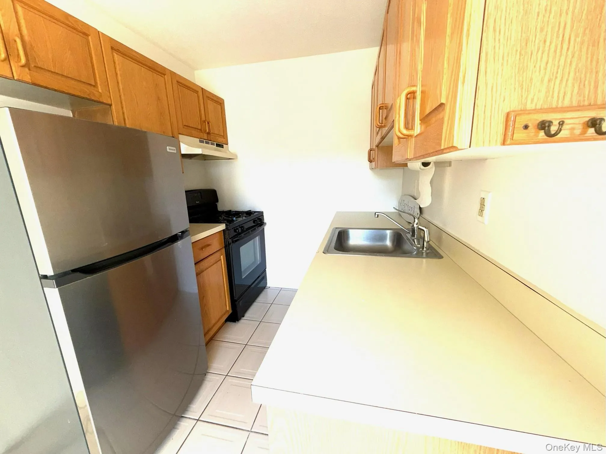 Kitchen featuring freestanding refrigerator, black gas range, light countertops, light tile patterned flooring, and under cabinet range hood Kitchen featuring freestanding refrigerator, black gas range, light countertops, light tile patterned flooring, and under cabinet range hood