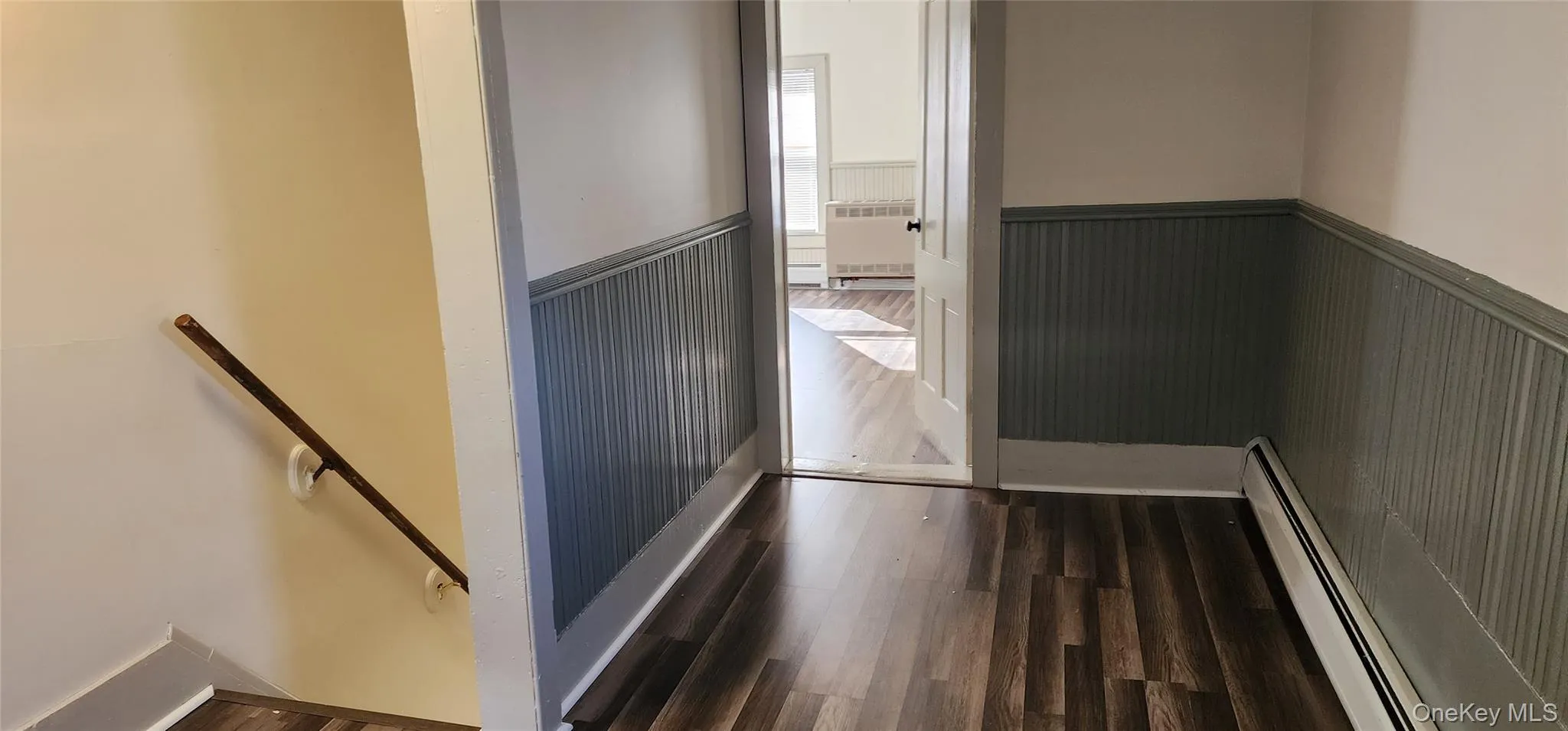 Hall featuring baseboard heating, a wainscoted wall, an upstairs landing, dark wood-style flooring, and radiator Hall featuring baseboard heating, a wainscoted wall, an upstairs landing, dark wood-style flooring, and radiator