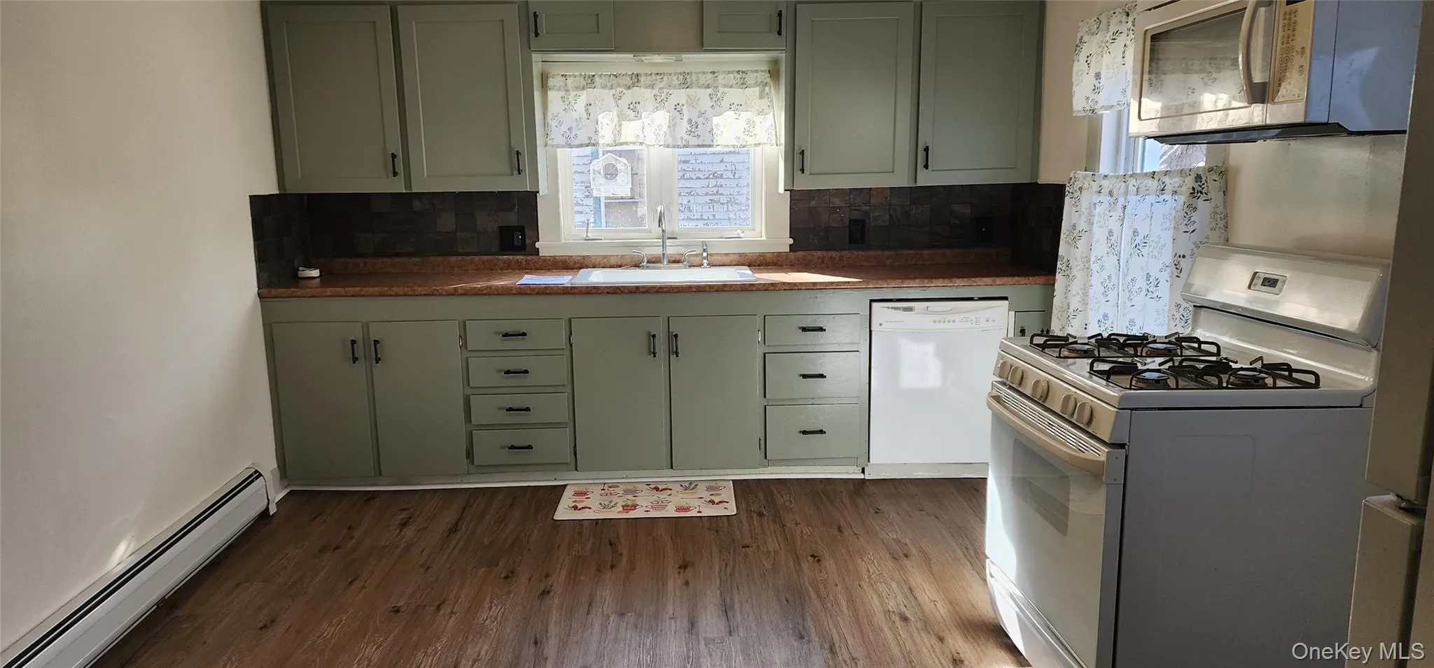 Kitchen featuring white appliances, a baseboard radiator, backsplash, dark wood finished floors, and green cabinetry Kitchen featuring white appliances, a baseboard radiator, backsplash, dark wood finished floors, and green cabinetry