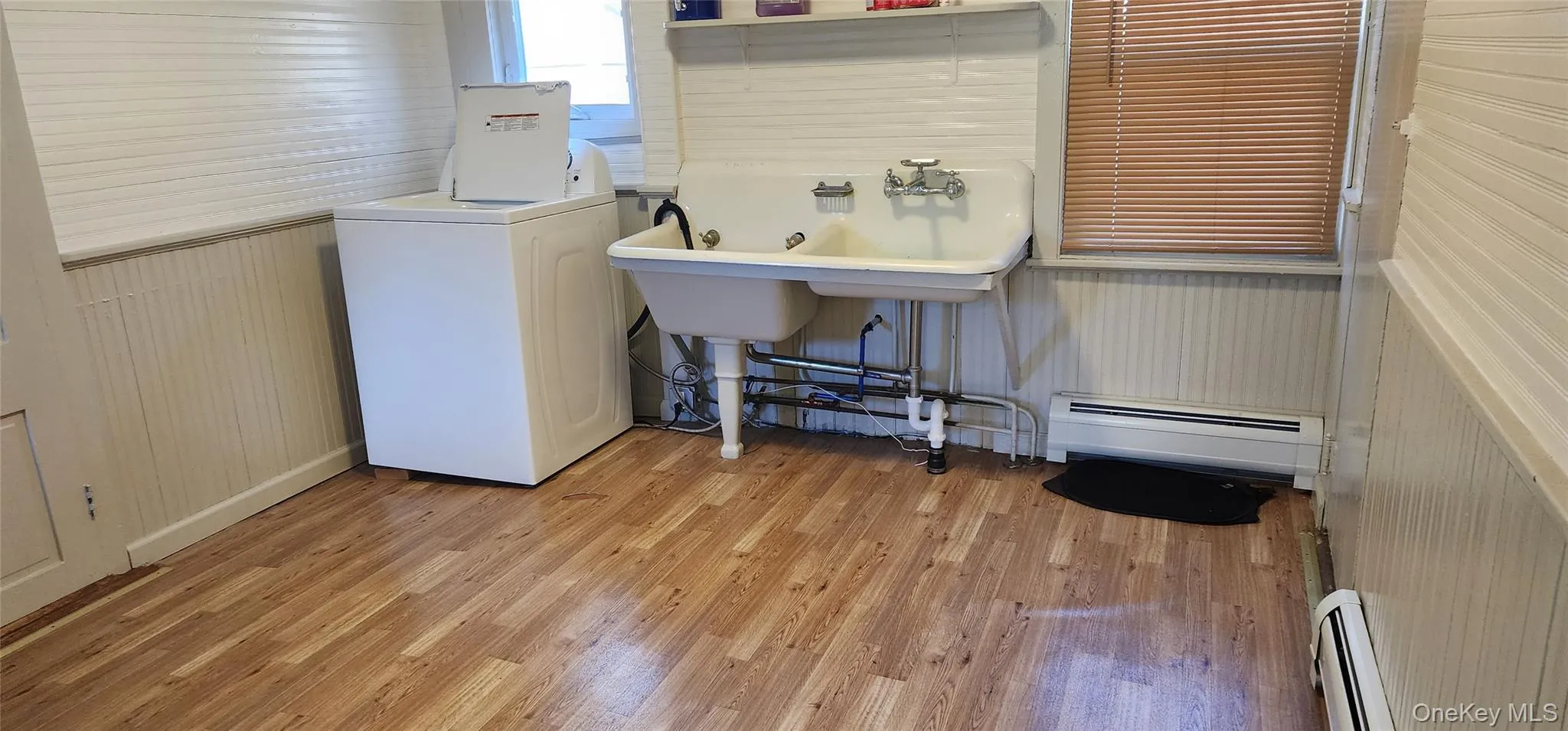 Washroom with washer / clothes dryer, baseboard heating, light wood-type flooring, and wooden walls Washroom with washer / clothes dryer, baseboard heating, light wood-type flooring, and wooden walls