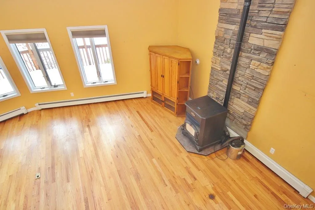 Spare room featuring a wood stove, a baseboard radiator, and light wood-type flooring Spare room featuring a wood stove, a baseboard radiator, and light wood-type flooring