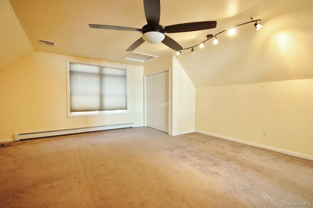 Additional living space featuring vaulted ceiling, attic access, baseboard heating, light carpet, and ceiling fan Additional living space featuring vaulted ceiling, attic access, baseboard heating, light carpet, and ceiling fan