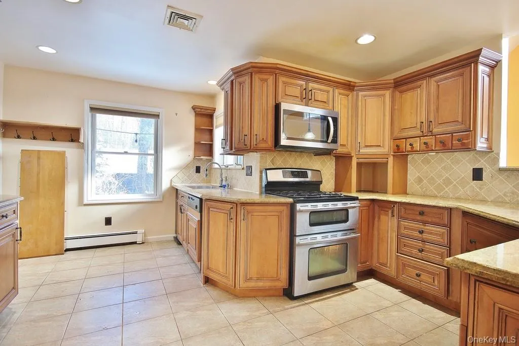 Kitchen featuring appliances with stainless steel finishes, brown cabinetry, a baseboard heating unit, light tile patterned flooring, and recessed lighting Kitchen featuring appliances with stainless steel finishes, brown cabinetry, a baseboard heating unit, light tile patterned flooring, and recessed lighting