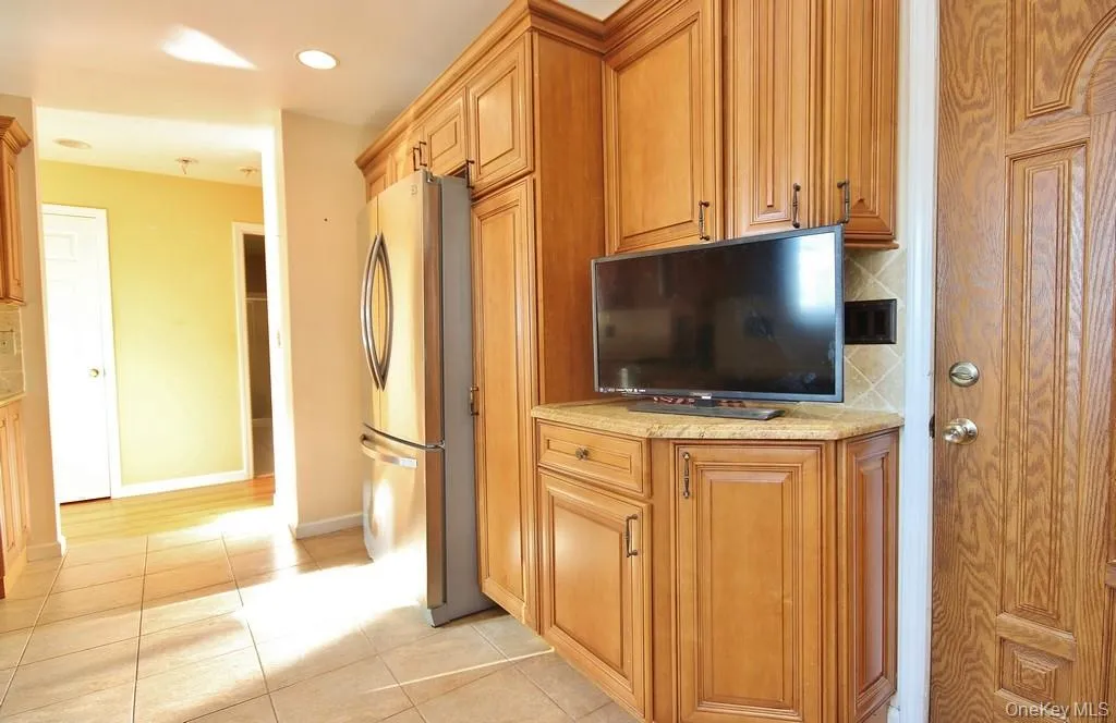 Kitchen featuring decorative backsplash, freestanding refrigerator, light stone counters, brown cabinetry, and light tile patterned floors Kitchen featuring decorative backsplash, freestanding refrigerator, light stone counters, brown cabinetry, and light tile patterned floors