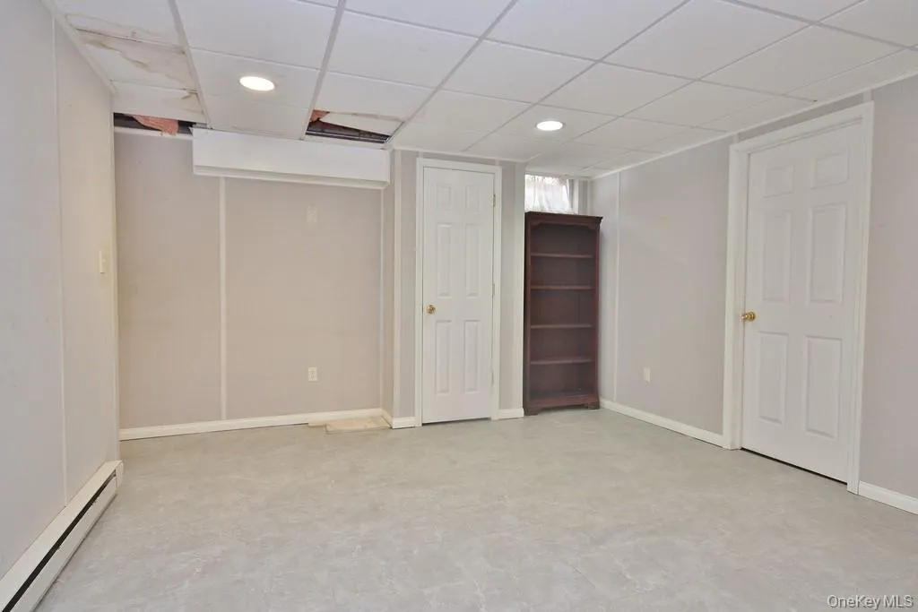 Finished basement with a baseboard heating unit, recessed lighting, a drop ceiling, and light floors Finished basement with a baseboard heating unit, recessed lighting, a drop ceiling, and light floors