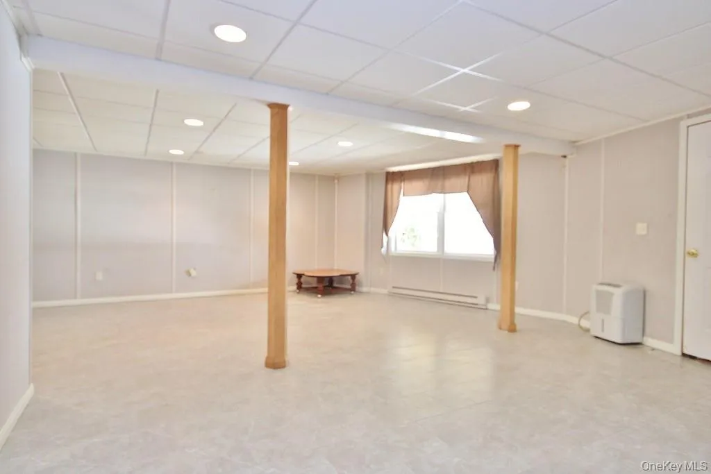 Basement featuring a drop ceiling, a baseboard heating unit, recessed lighting, and light flooring Basement featuring a drop ceiling, a baseboard heating unit, recessed lighting, and light flooring