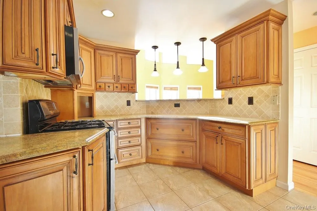 Kitchen with gas stove, brown cabinetry, pendant lighting, light stone countertops, and recessed lighting Kitchen with gas stove, brown cabinetry, pendant lighting, light stone countertops, and recessed lighting