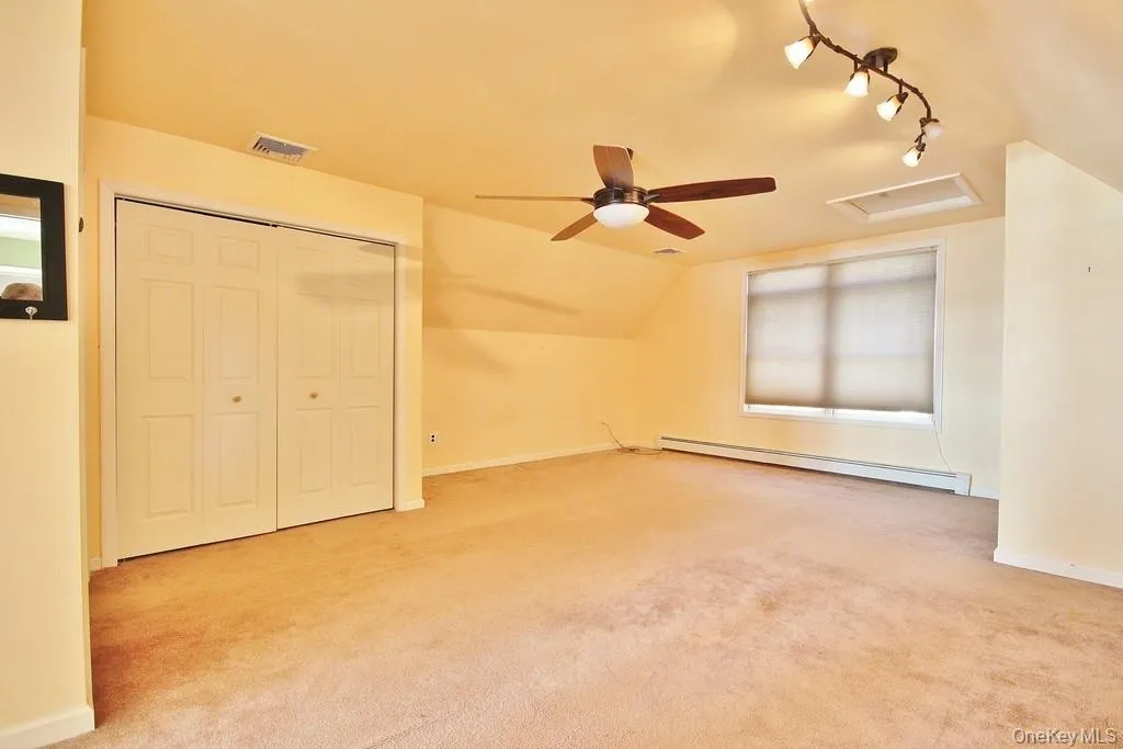 Bonus room featuring attic access, a baseboard heating unit, lofted ceiling, light carpet, and ceiling fan Bonus room featuring attic access, a baseboard heating unit, lofted ceiling, light carpet, and ceiling fan