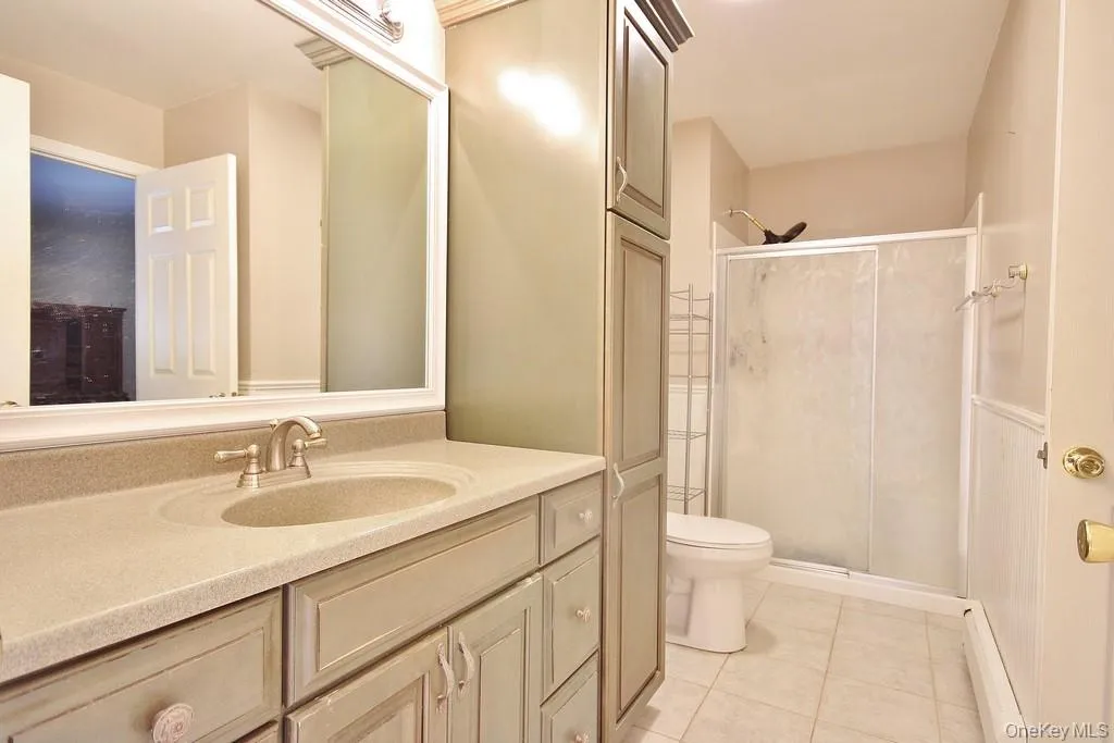 Bathroom featuring vanity, a stall shower, a baseboard heating unit, and light tile patterned flooring Bathroom featuring vanity, a stall shower, a baseboard heating unit, and light tile patterned flooring