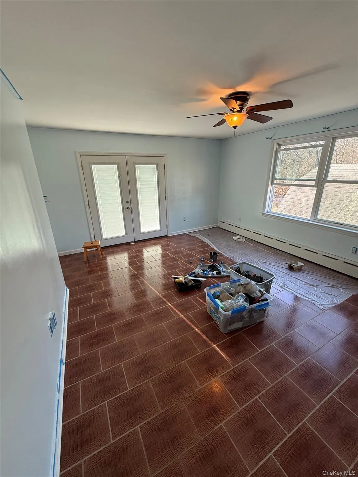 living room featuring a baseboard heating, French doors, and ceiling fan. (being painted) living room featuring a baseboard heating, French doors, and ceiling fan. (being painted)