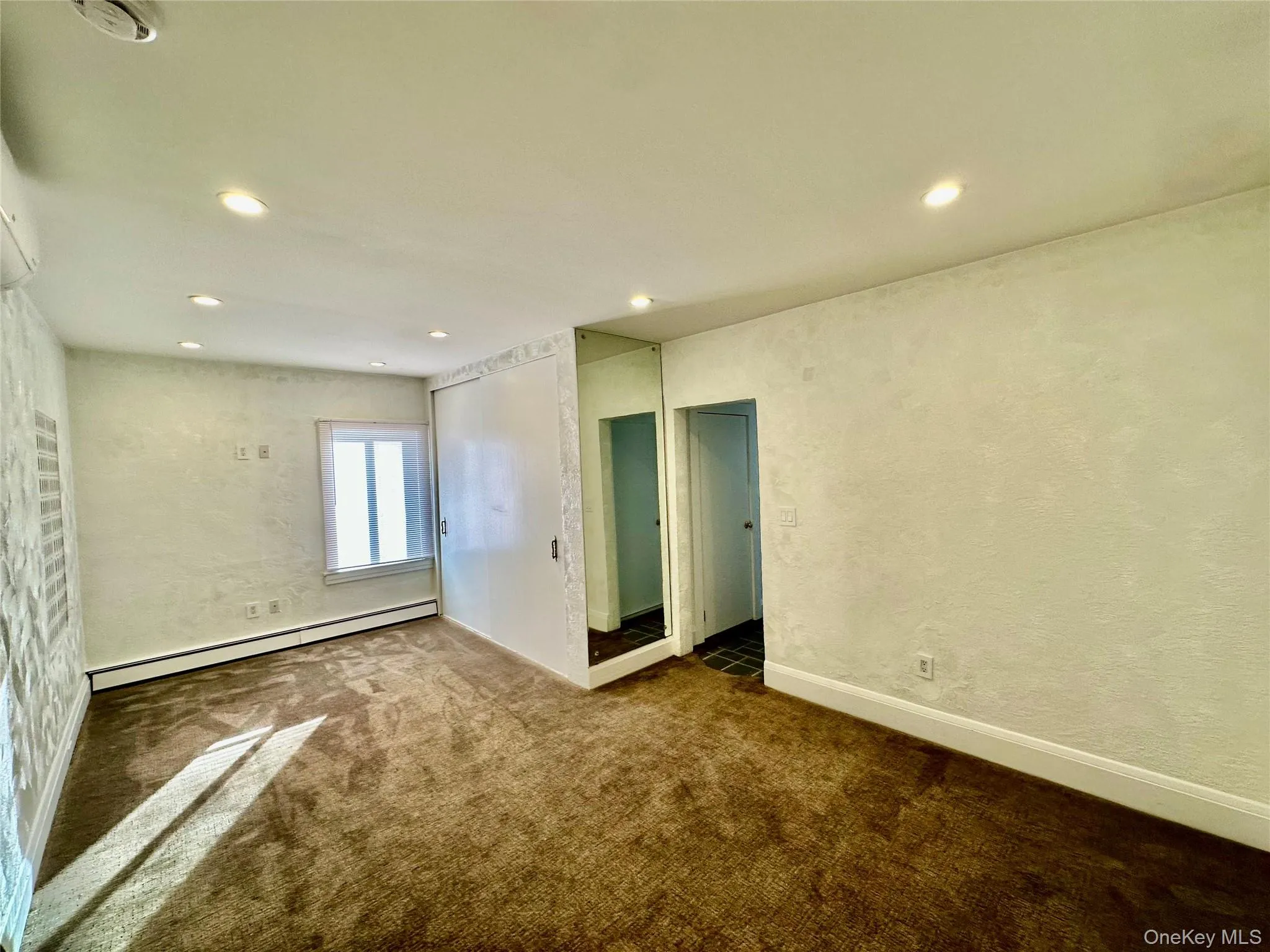 Empty room featuring a textured wall, a baseboard heating unit, recessed lighting, and carpet Empty room featuring a textured wall, a baseboard heating unit, recessed lighting, and carpet