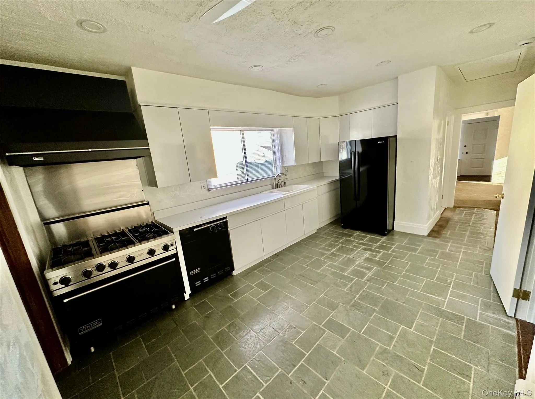 Kitchen with light countertops, black appliances, modern cabinets, white cabinetry, and ventilation hood Kitchen with light countertops, black appliances, modern cabinets, white cabinetry, and ventilation hood