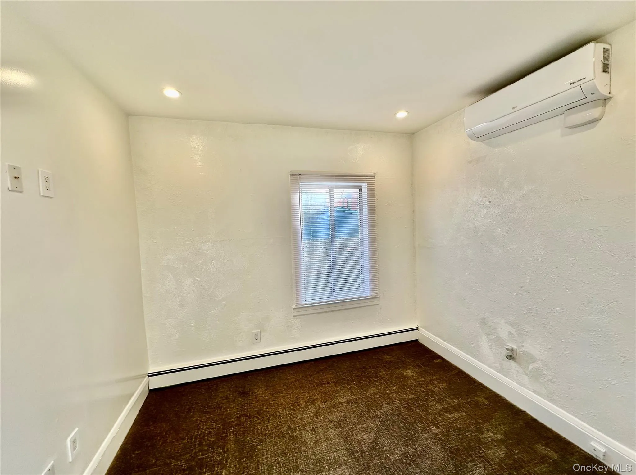Unfurnished room with a wall mounted AC, baseboard heating, dark carpet, recessed lighting, and a textured wall Unfurnished room with a wall mounted AC, baseboard heating, dark carpet, recessed lighting, and a textured wall