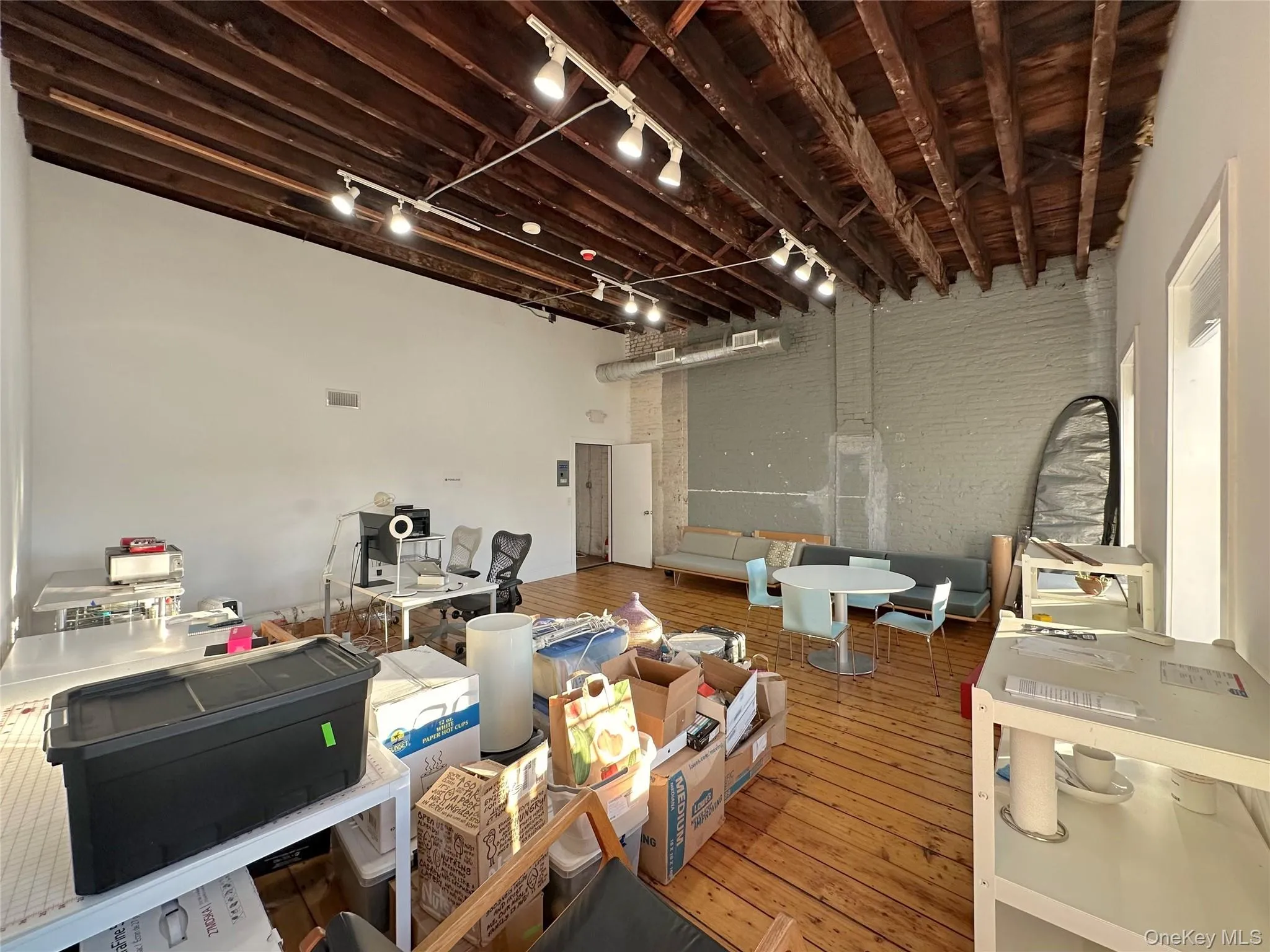 Misc room featuring track lighting, wood-type flooring, brick wall, an office area, and a high ceiling Misc room featuring track lighting, wood-type flooring, brick wall, an office area, and a high ceiling