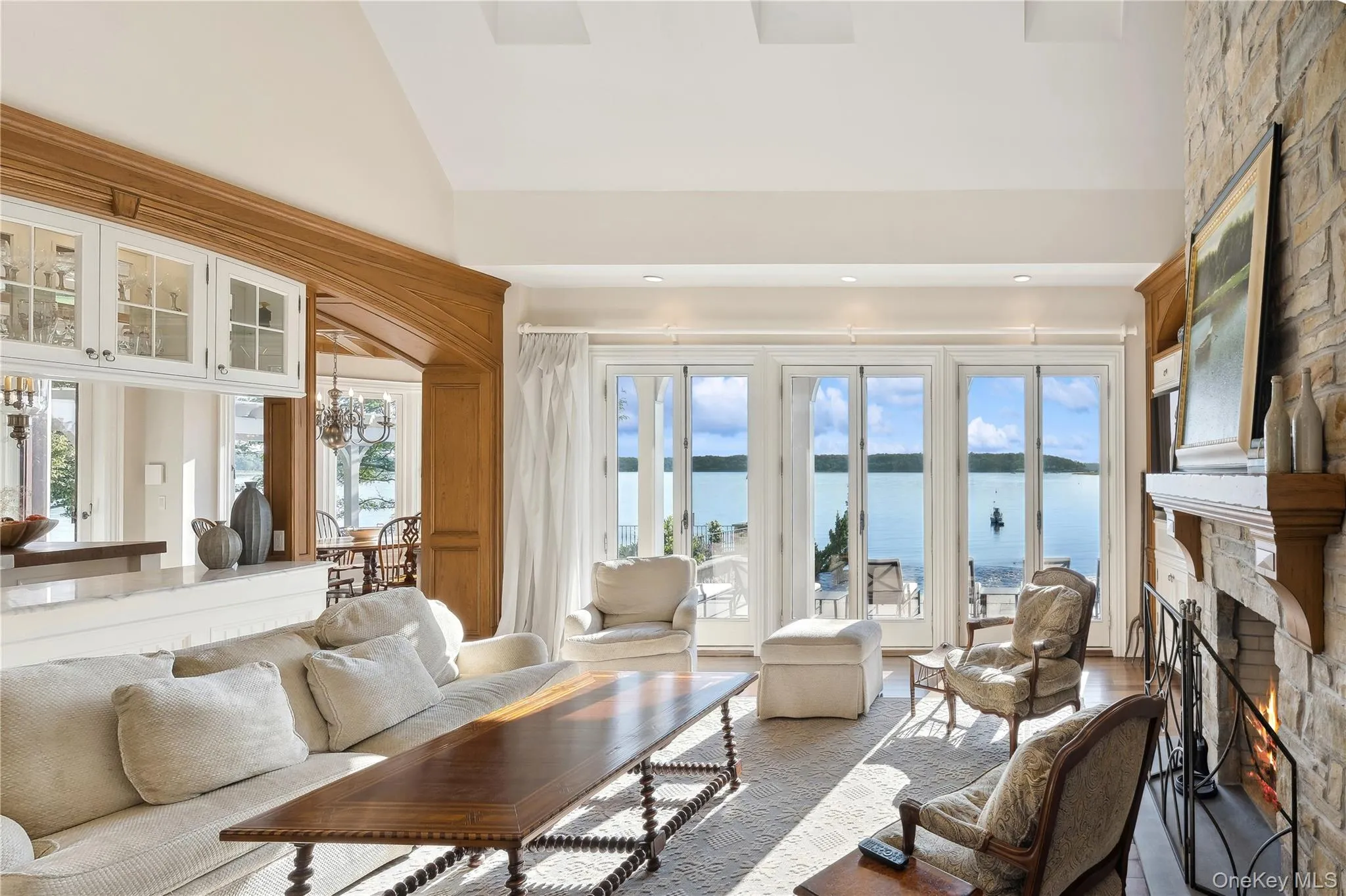Living room with a water view, a large fireplace, high vaulted ceiling, and recessed lighting Living room with a water view, a large fireplace, high vaulted ceiling, and recessed lighting