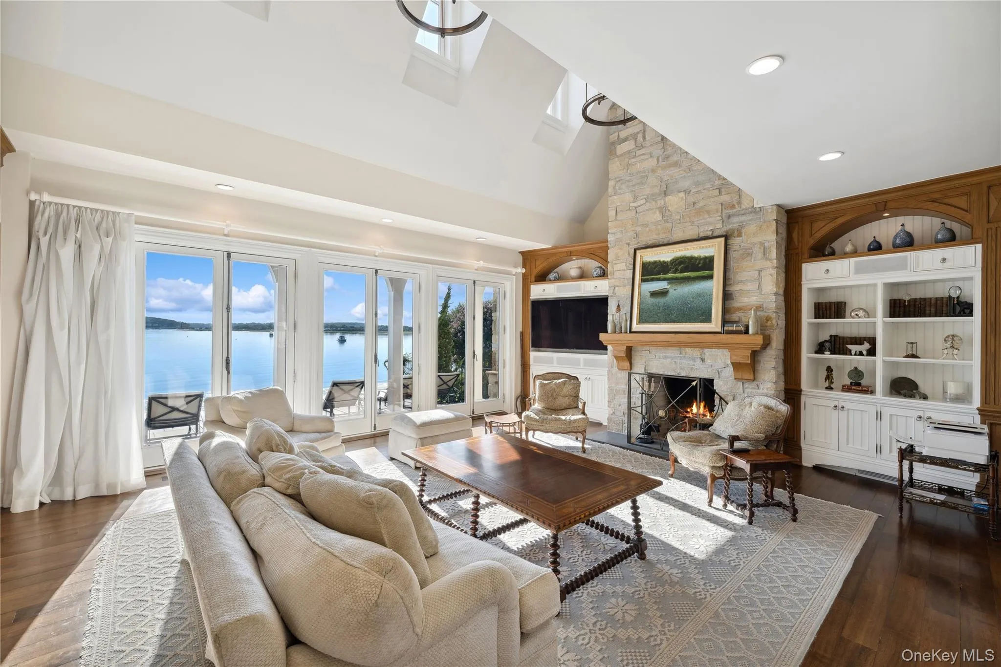 Living area with built in features, a stone fireplace, dark wood-type flooring, high vaulted ceiling, and recessed lighting Living area with built in features, a stone fireplace, dark wood-type flooring, high vaulted ceiling, and recessed lighting