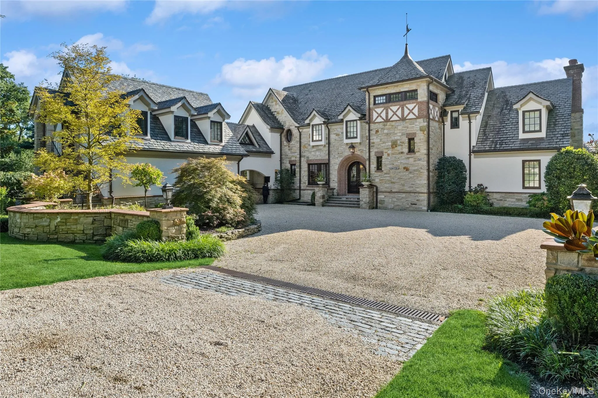 View of front facade featuring a high end roof, curved driveway, stucco siding, stone siding, and a chimney View of front facade featuring a high end roof, curved driveway, stucco siding, stone siding, and a chimney